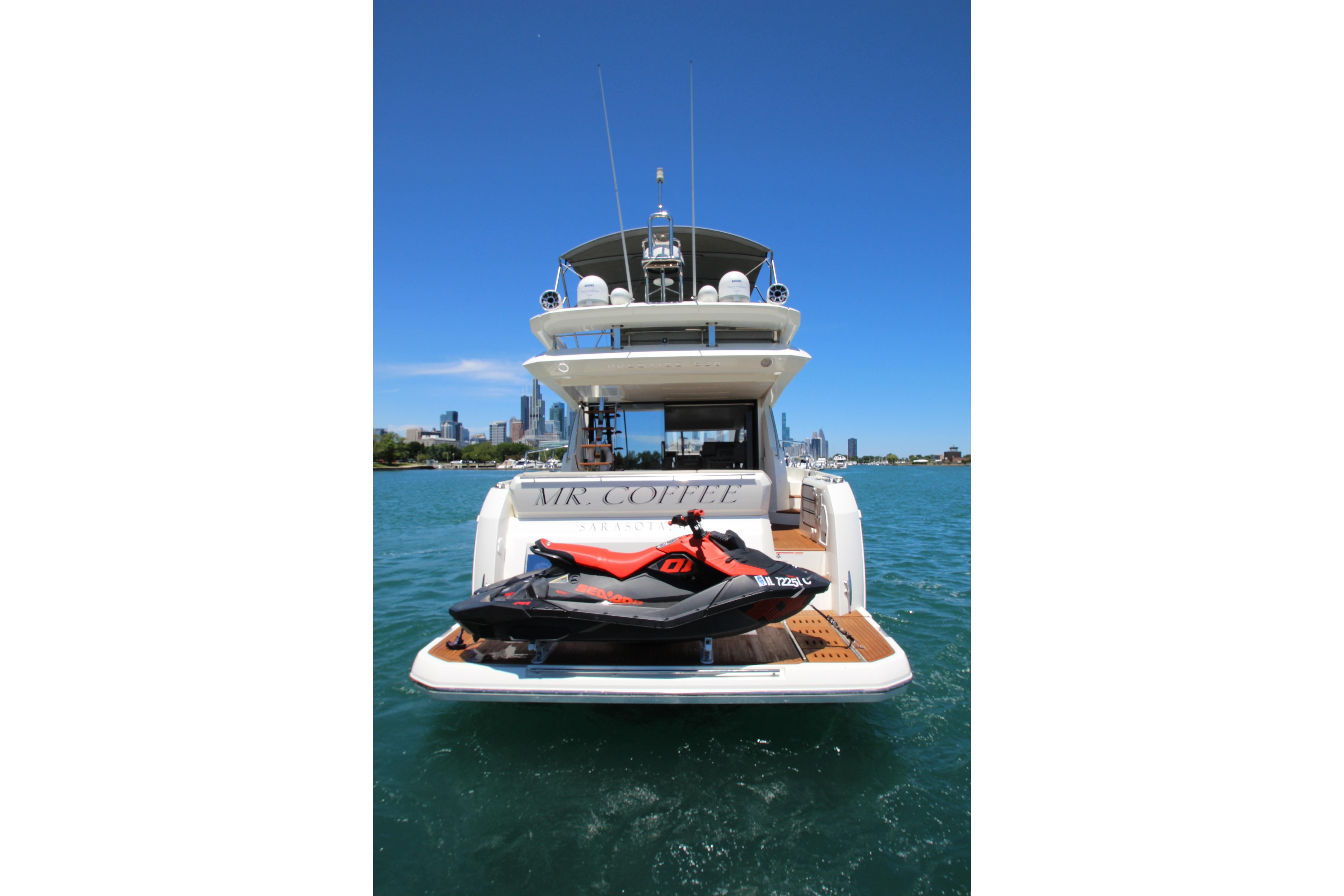 Luxury 2022 Prestige 520 yacht with jet ski on deck, city skyline in background.