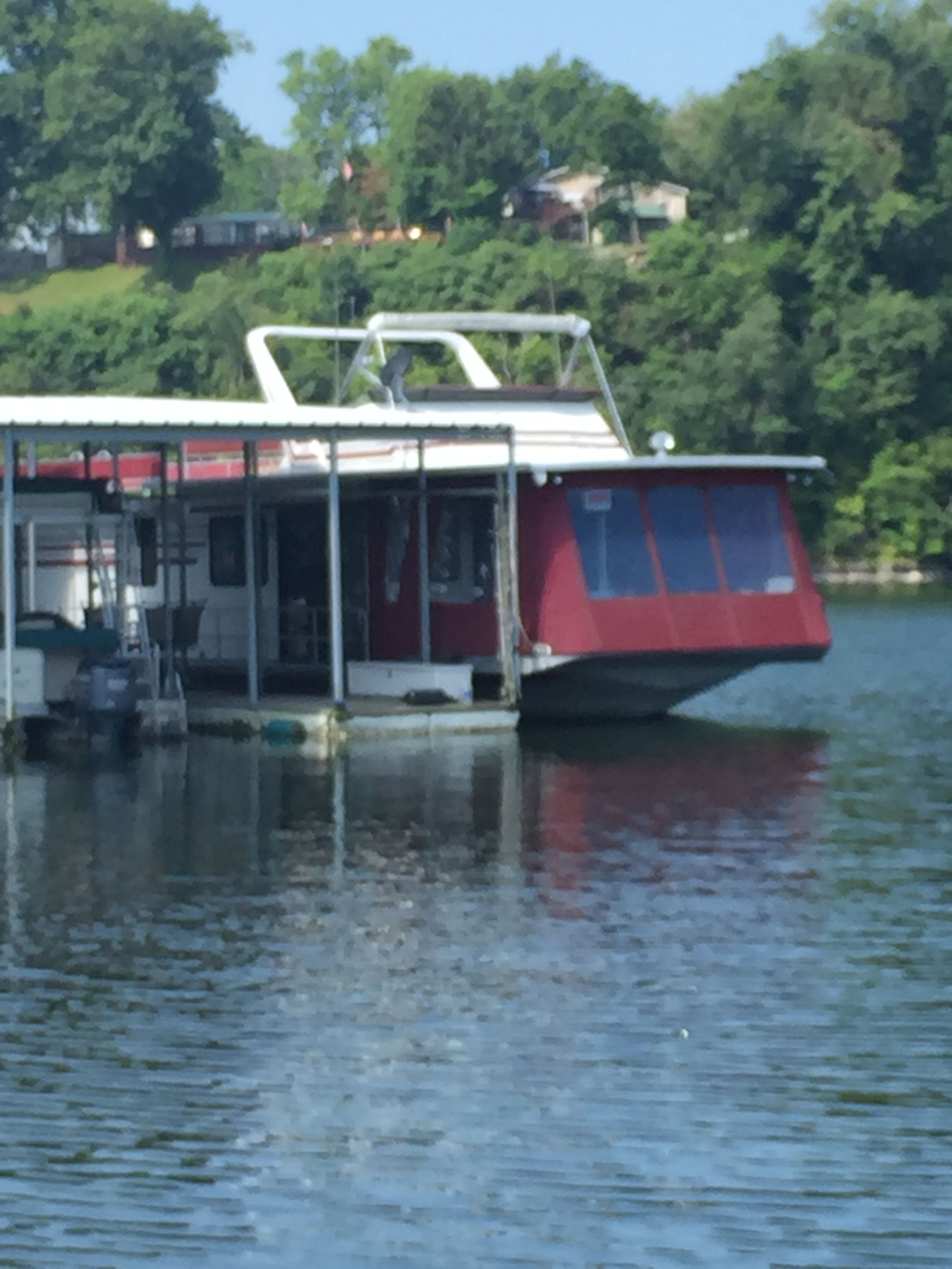 A red 1989 Sumerset houseboat docked at a tranquil lakeside.