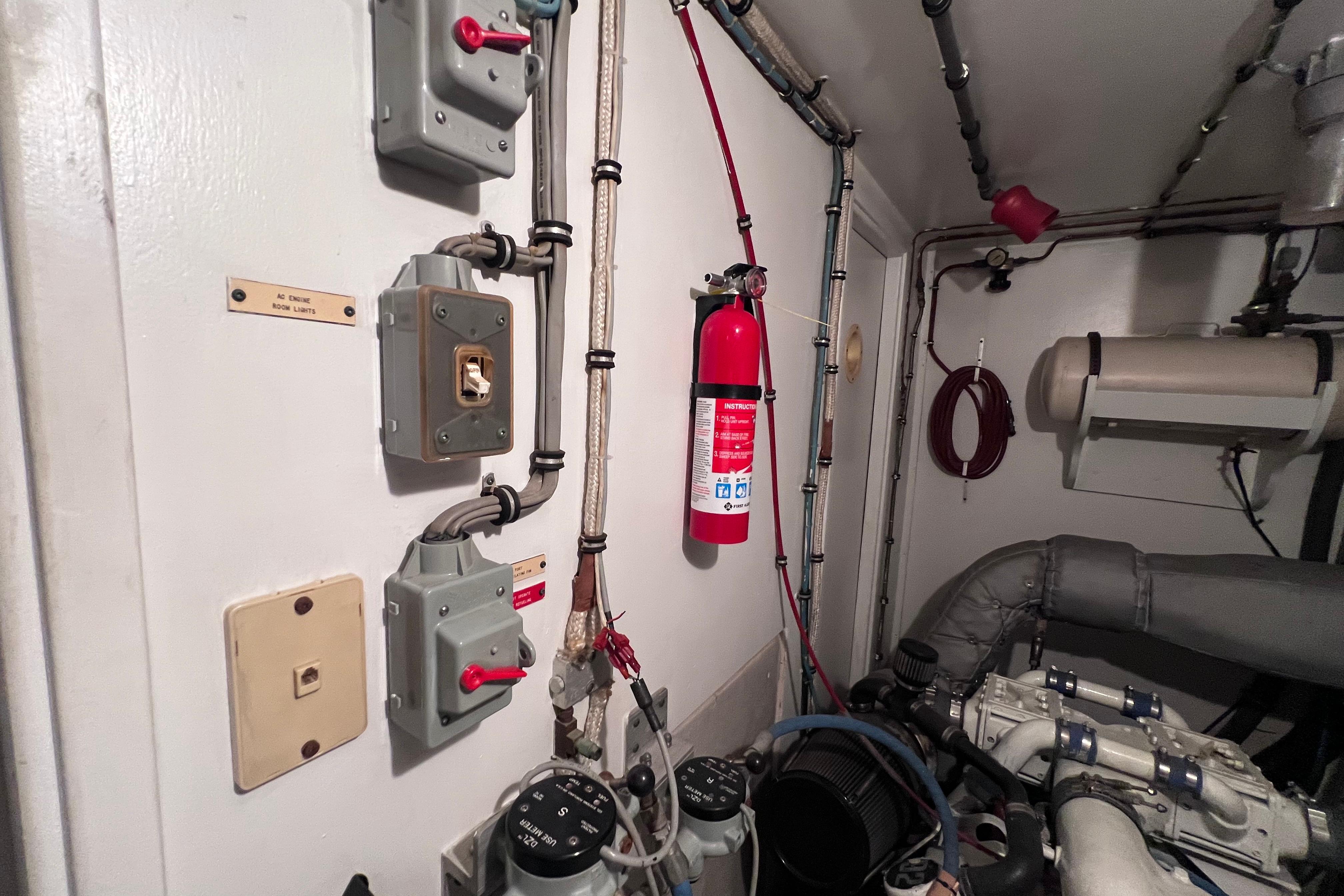 Engine room of 1987 Hatteras 70 Cockpit Motor Yacht with fire extinguisher and control panels.