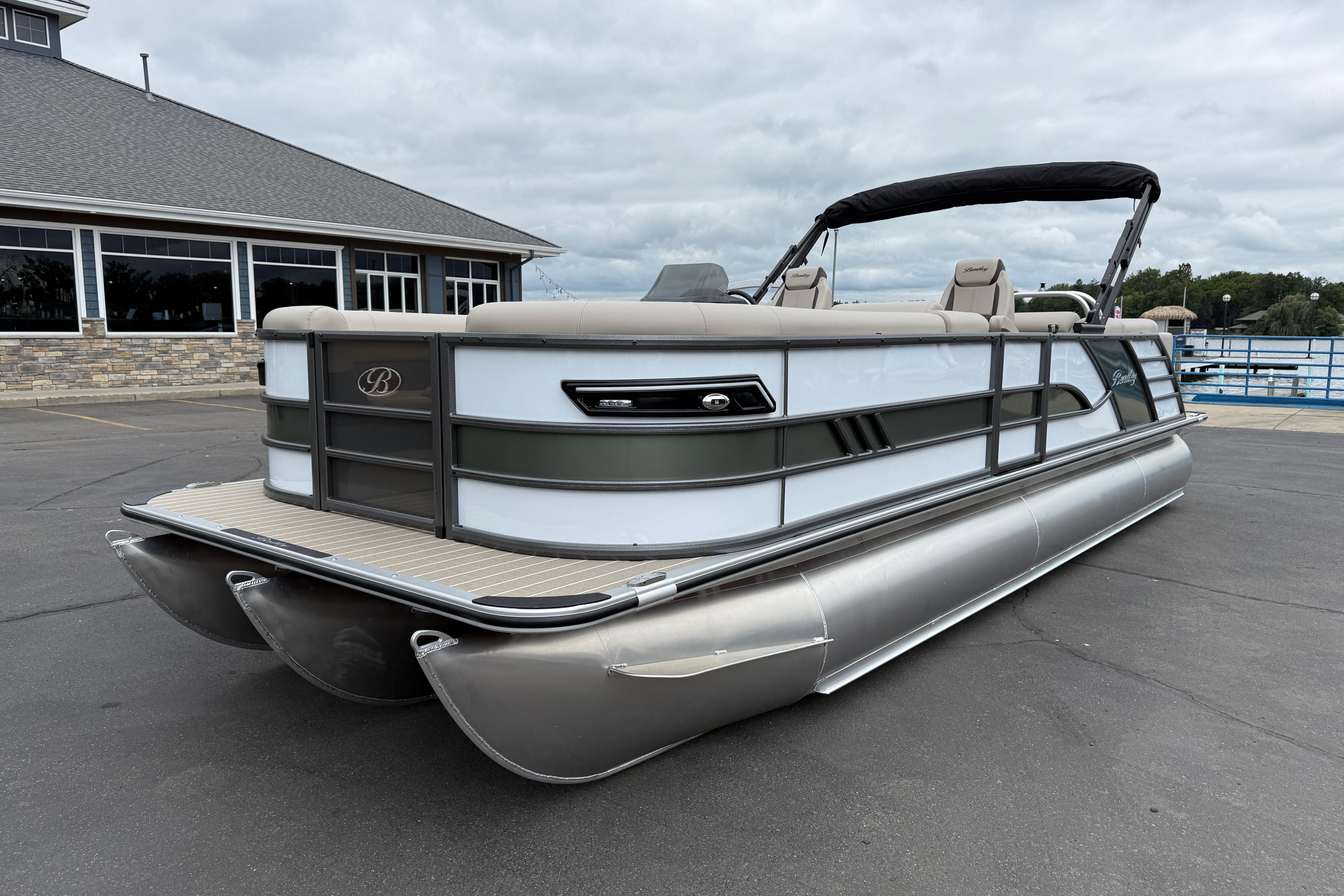 2026 Bentley Pontoons Elite 253 Admiral, docked near a building under cloudy skies.