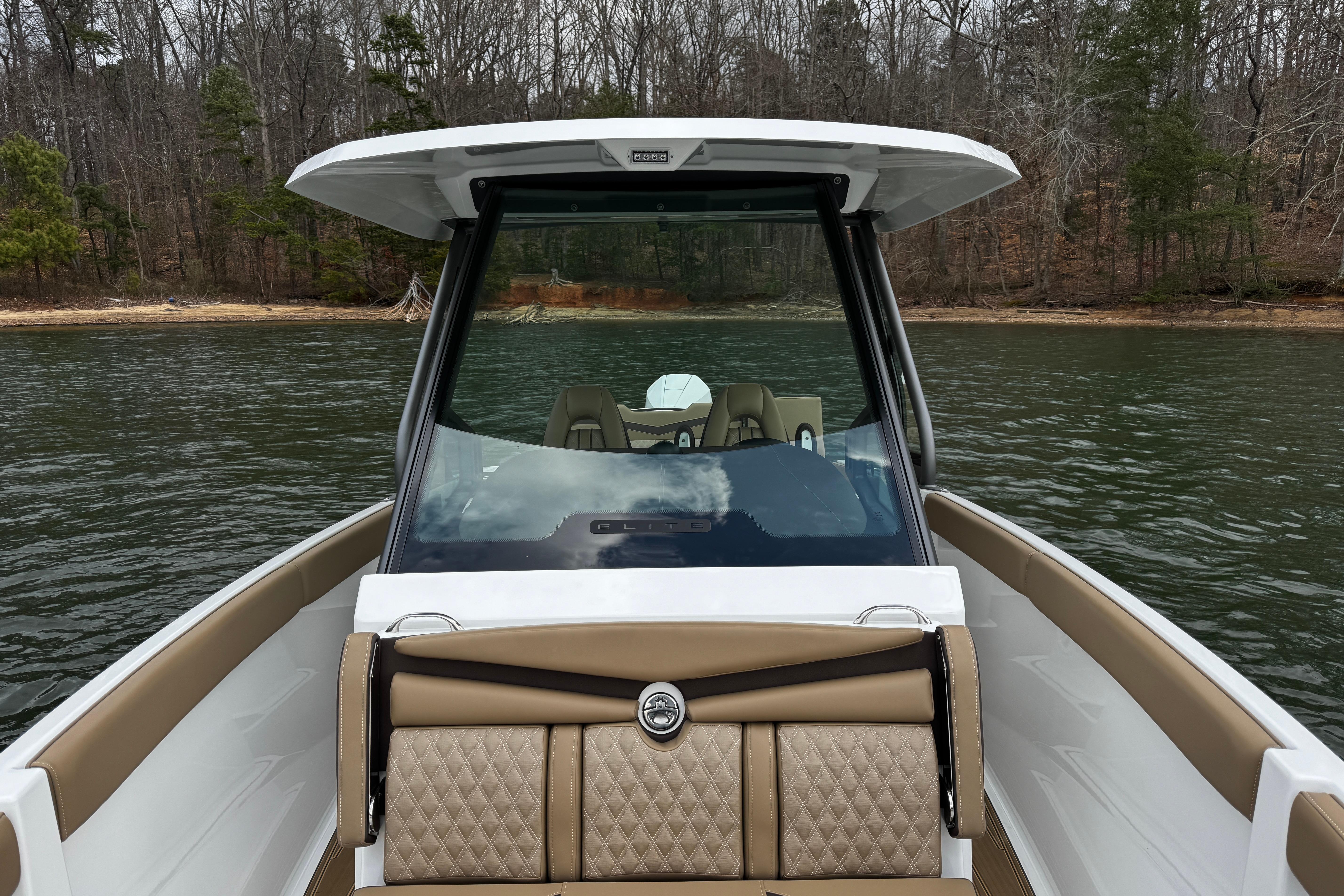 2026 Monterey Elite 25 OB boat on a calm lake with wooded shoreline.