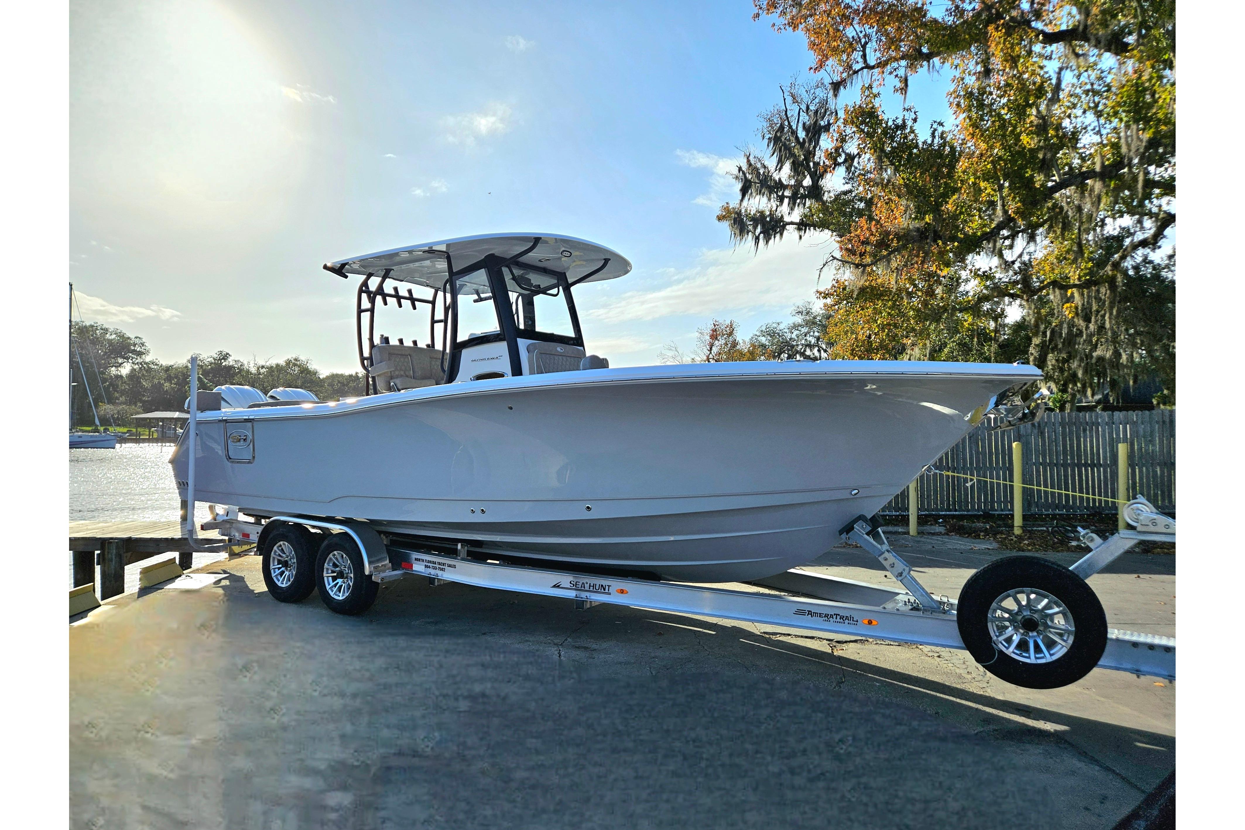 2026 Sea Hunt Ultra 285 SE boat on trailer, parked near water and trees.