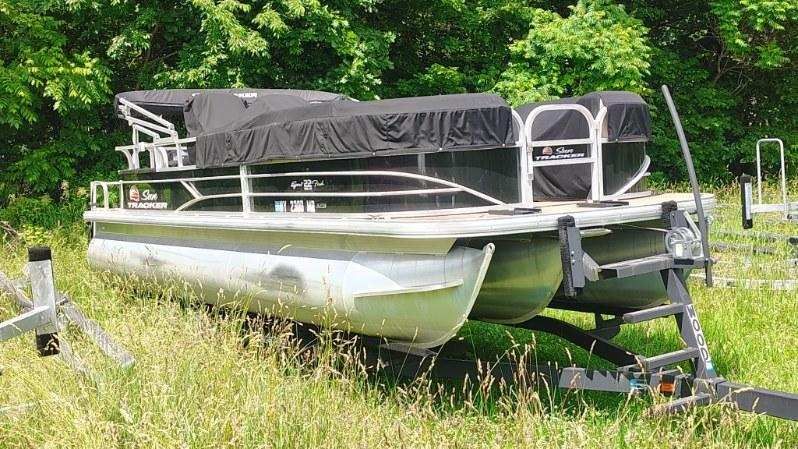A 2019 White River sf22xp3 pb bk pontoon boat sits on a trailer in the grass.