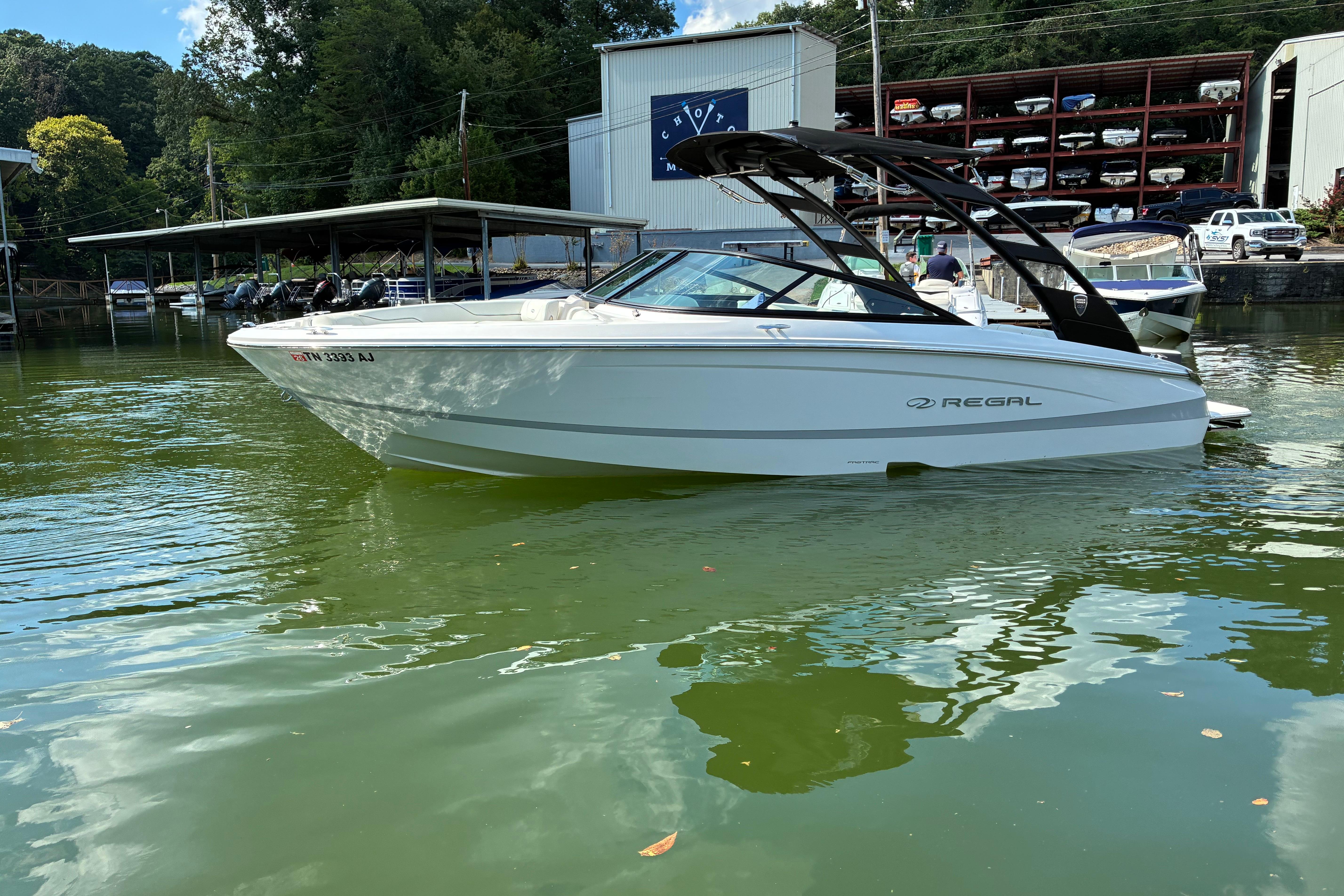2025 Regal LS2 boat on calm water near marina, surrounded by trees and buildings.