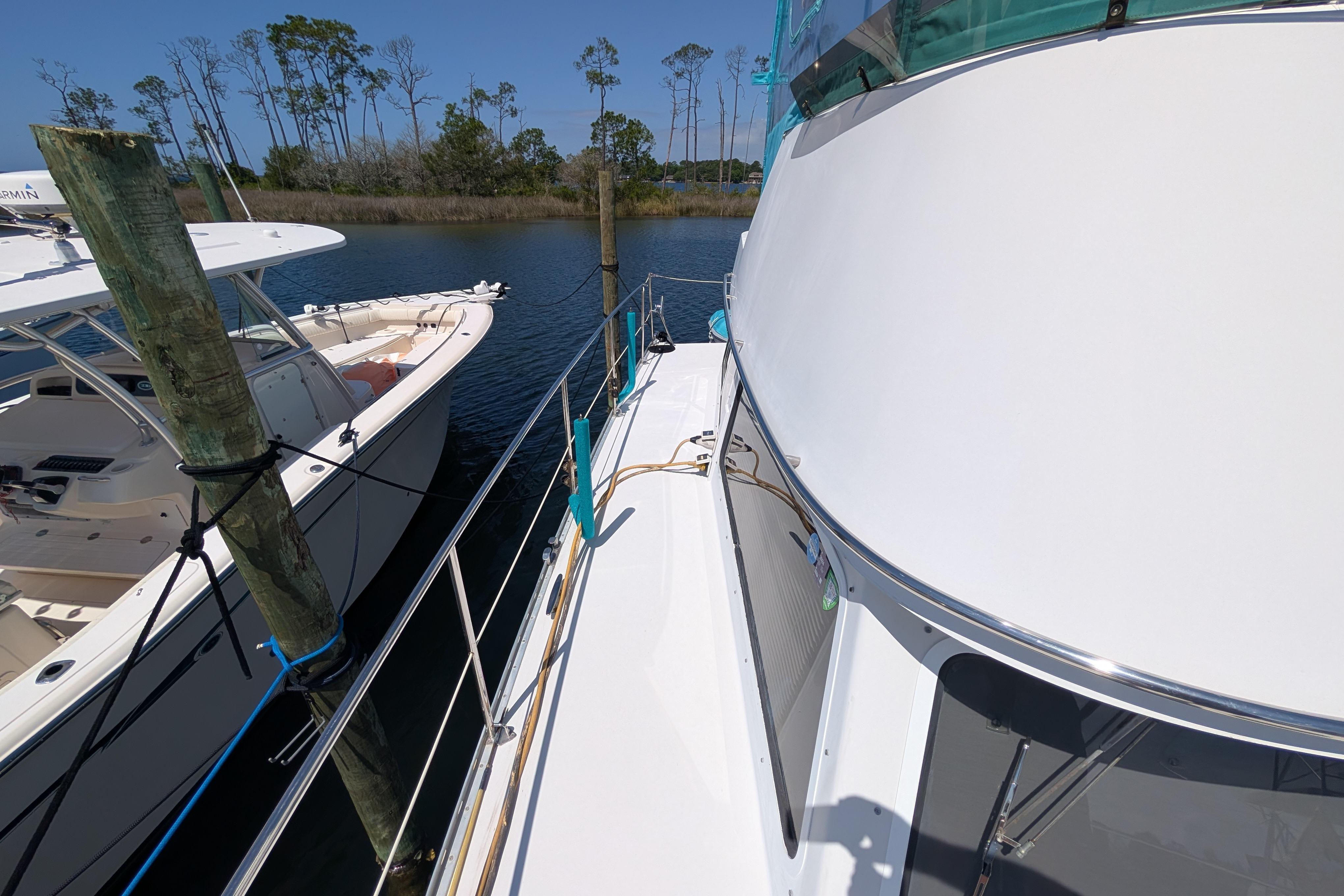 2004 PDQ 34 Powercat docked beside another boat, surrounded by calm water and trees.