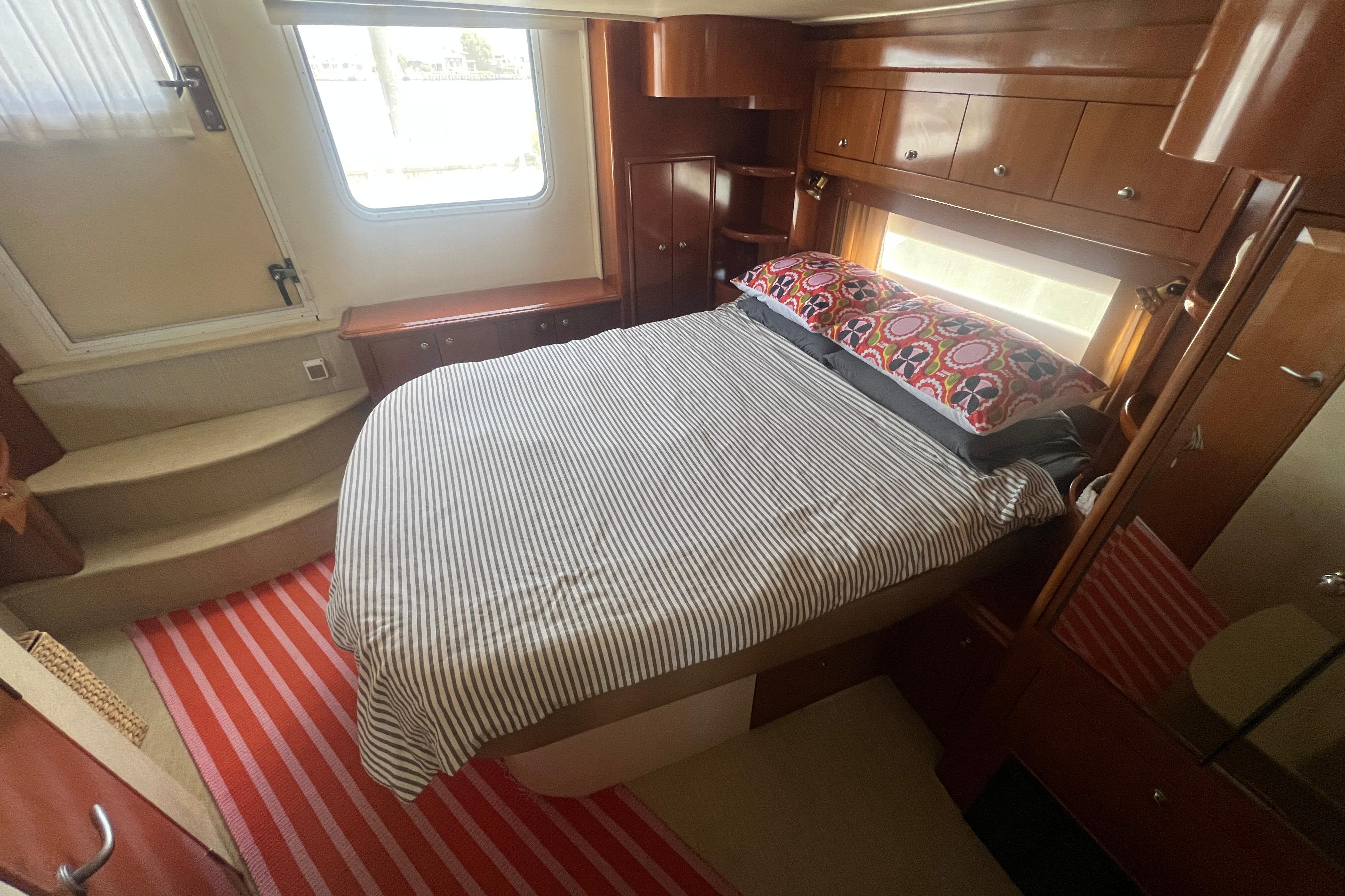 Interior of 2006 Carver 43 Motor Yacht bedroom with striped bedding and wooden cabinetry.