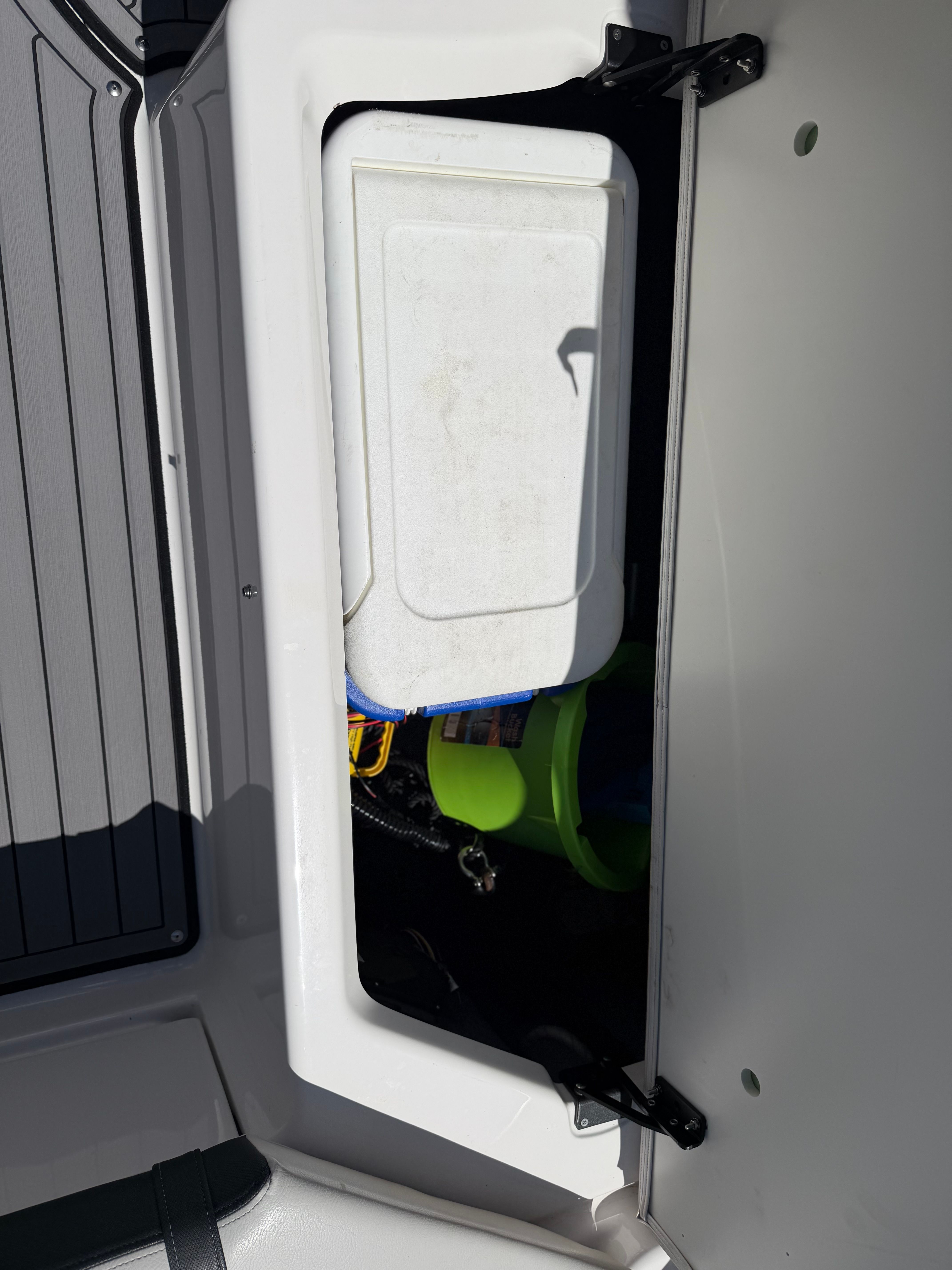 An open storage compartment on a boat with a white container and green buckets.