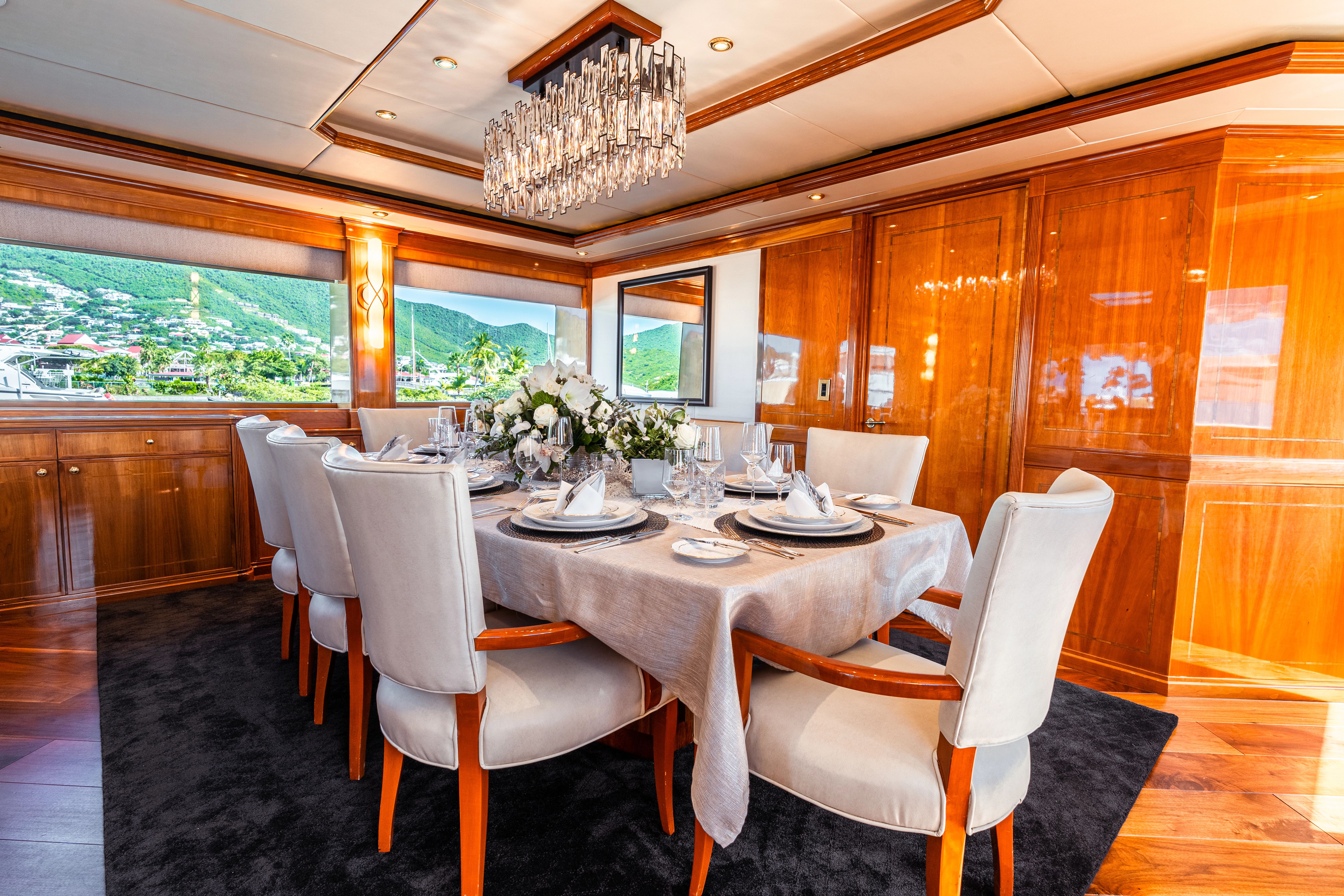Elegant dining area with wooden furniture and chandelier, surrounded by large windows overlooking the water.
