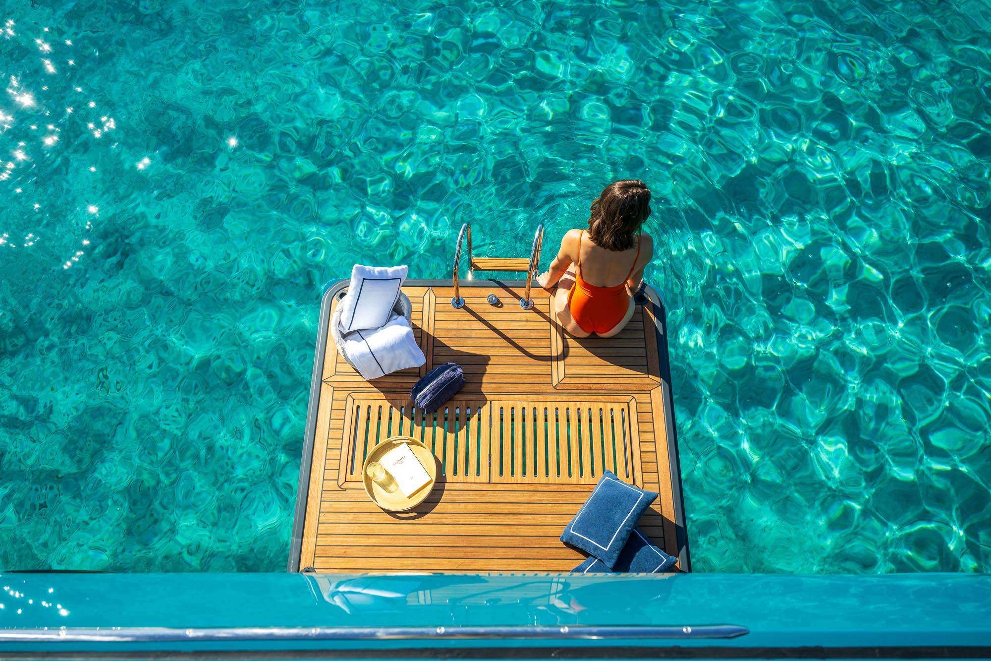 Woman relaxing on Lagoon Eighty 2 yacht platform, surrounded by clear turquoise water.