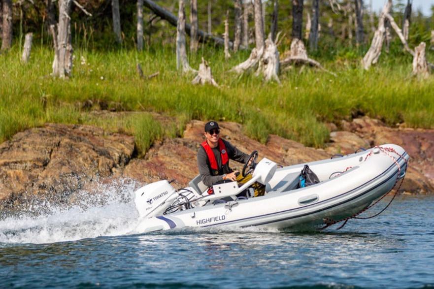 Person driving 2025 Highfield CL360 boat near rocky shoreline with trees.