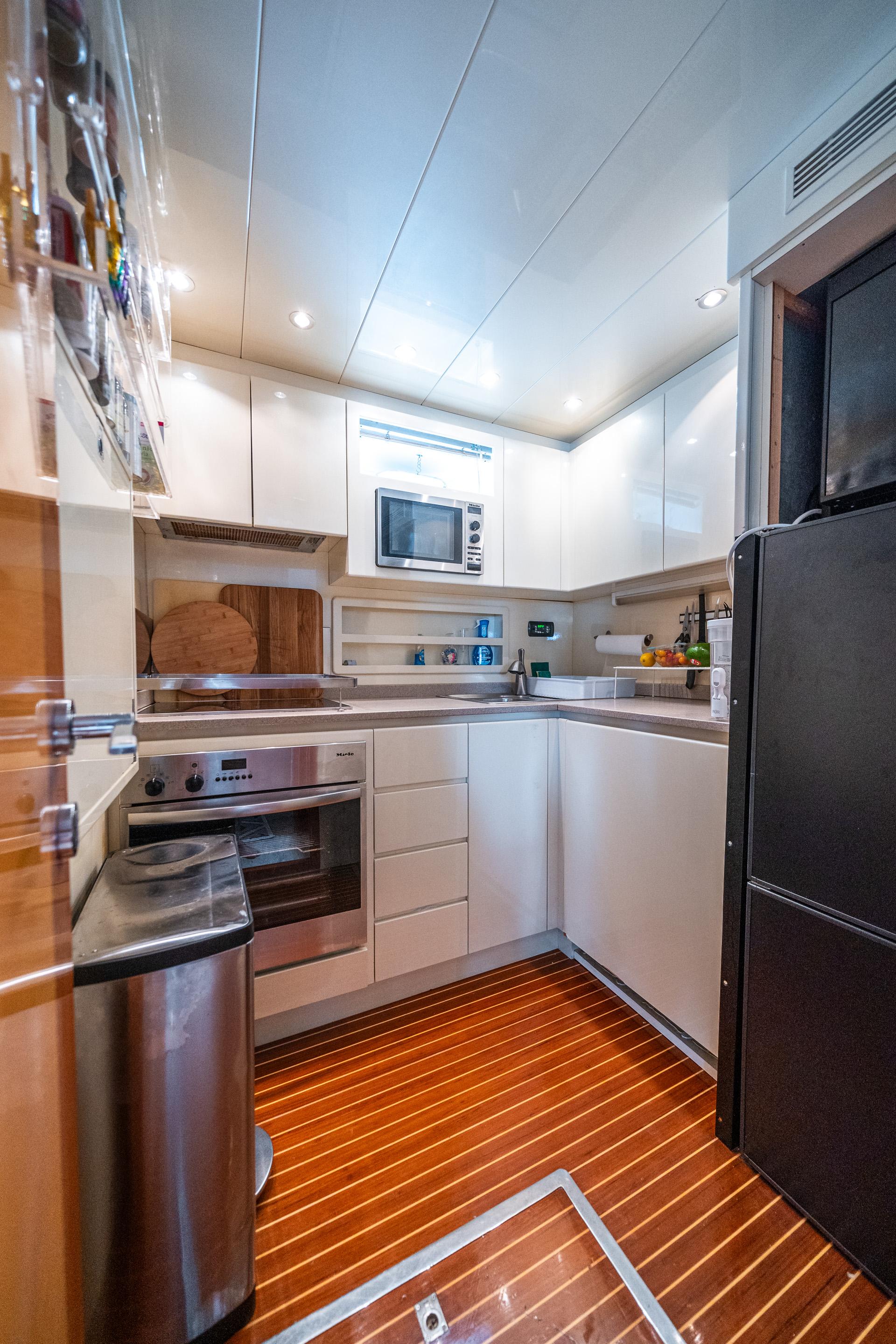 Modern kitchen interior in a 2001 Mangusta 80 yacht, featuring sleek white cabinetry and wood flooring.