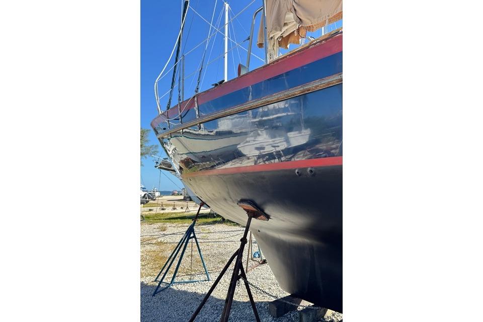 1989 Pacific Seacraft Crealock sailboat on stands, blue hull with red stripe, sunny day.