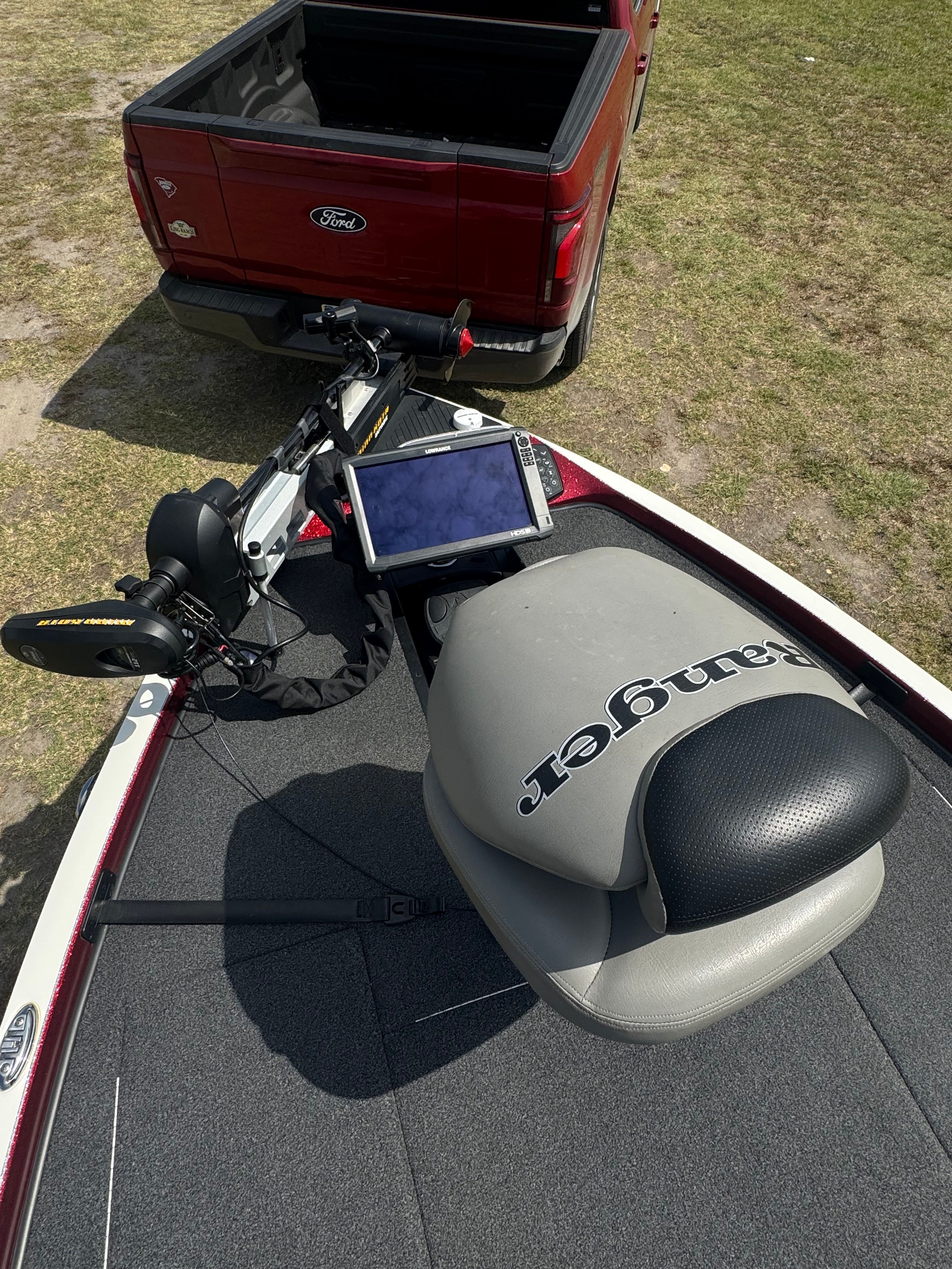 A Ranger boat with a seat and a screen, parked next to a red pickup truck.