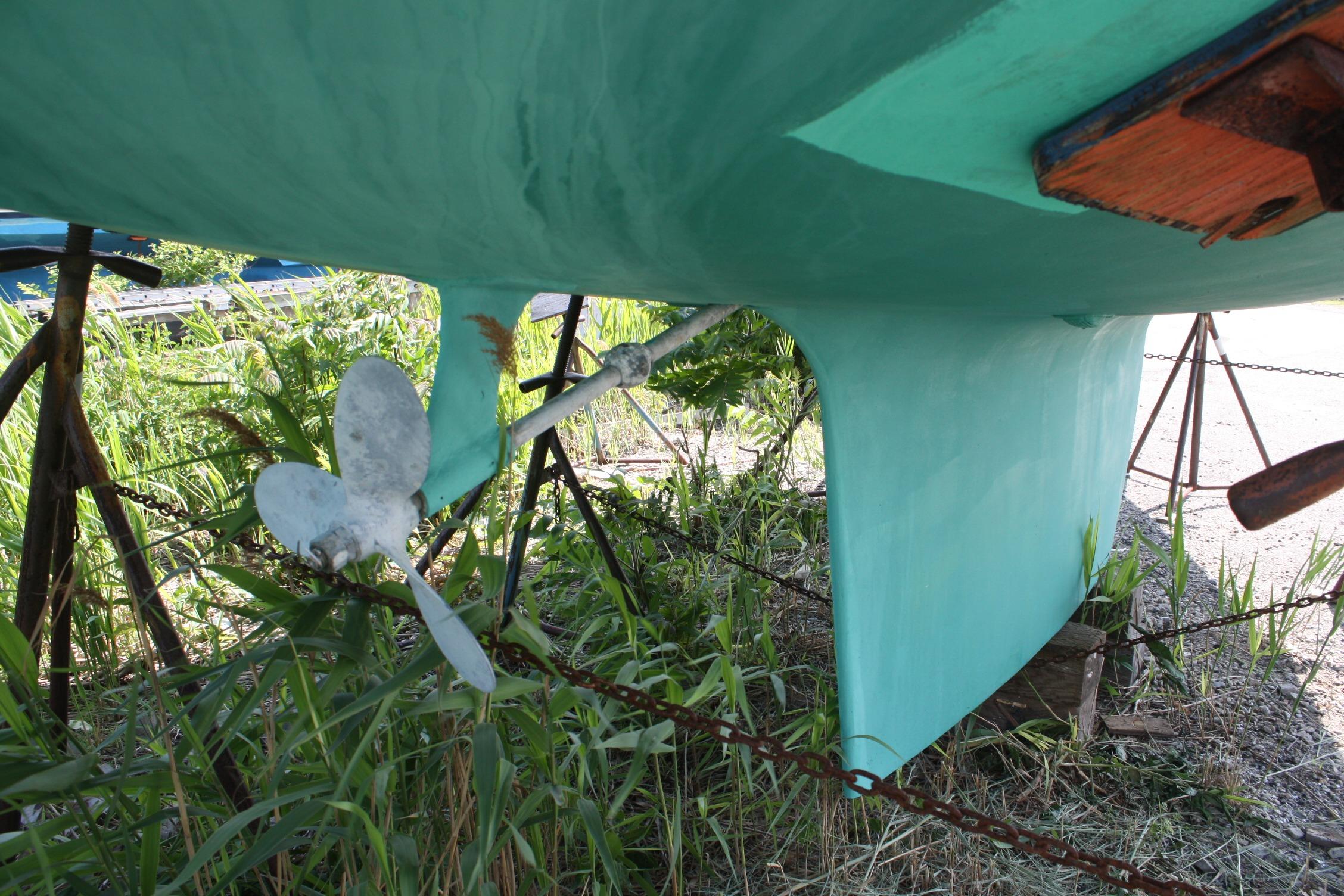 1981 S2 9.2A sailboat hull and propeller on stands, surrounded by greenery.
