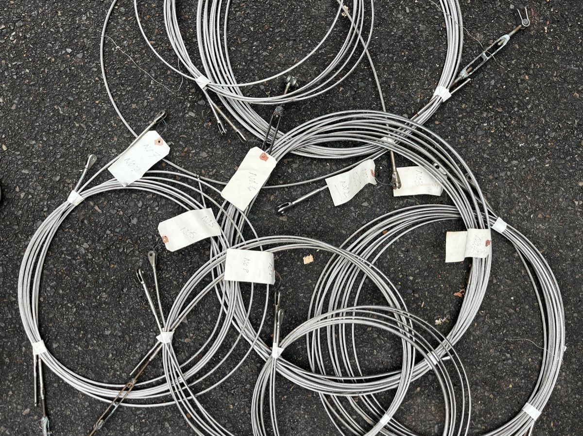 Several coiled steel cables with tags on asphalt.