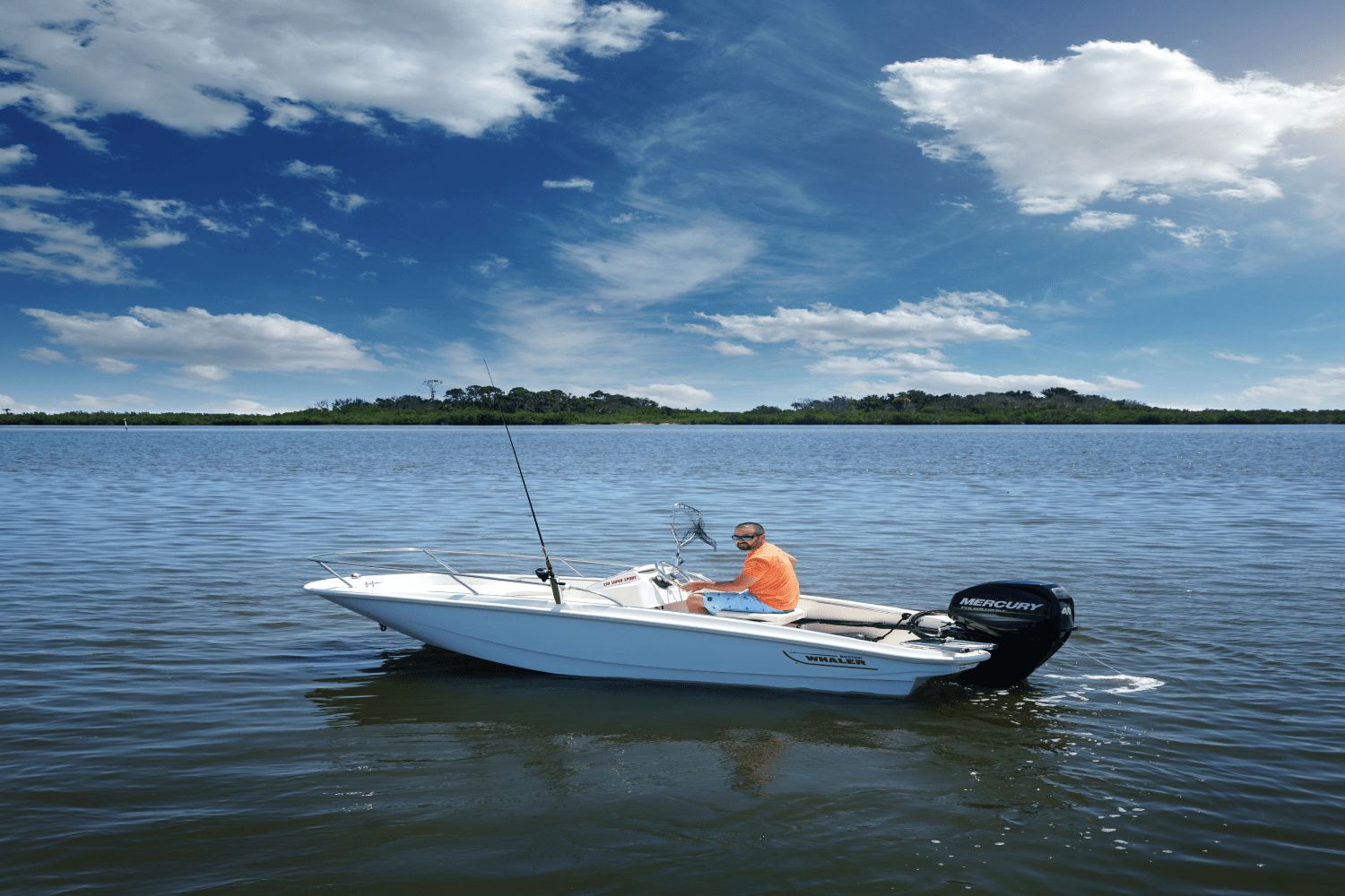 A man sits in a small white boat on calm water under a blue sky.