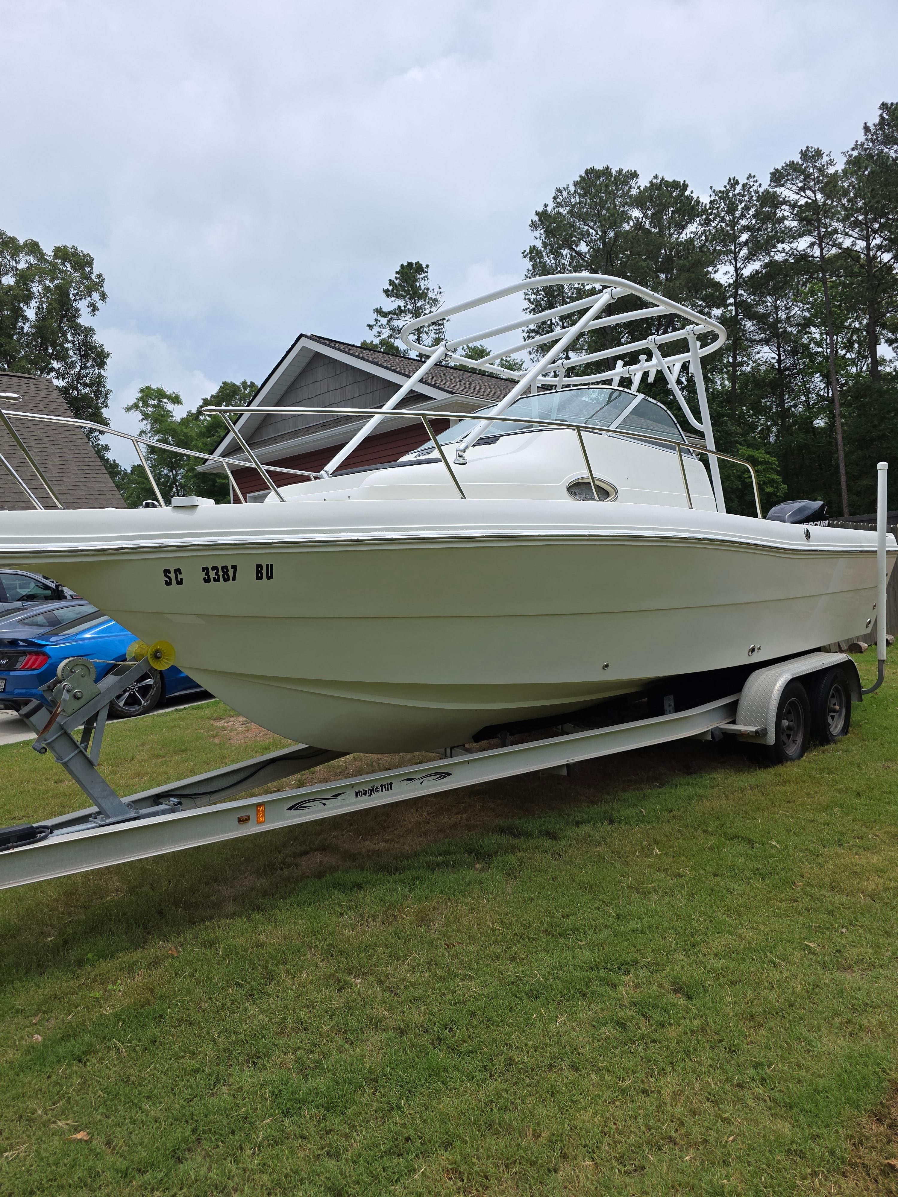 A white boat on a trailer, surrounded by trees and houses.