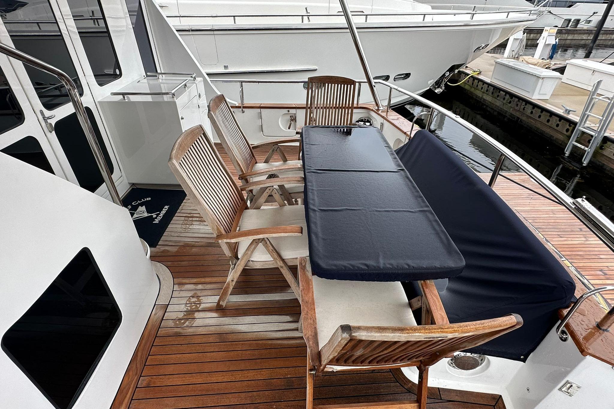 2023 Marlow Explorer 66E-CB yacht deck with wooden chairs and table, docked at marina.