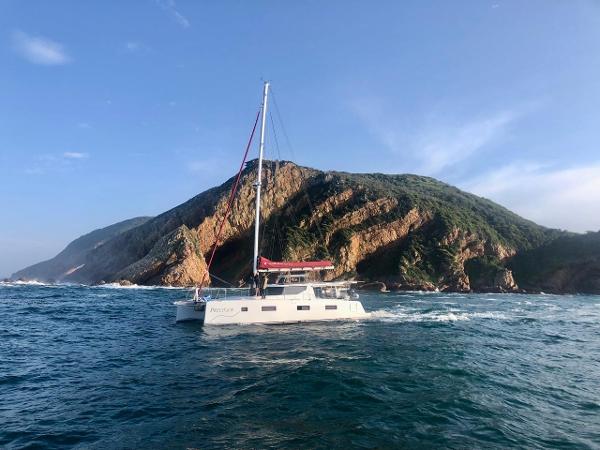 Sailboat Vision 444 cruising near rocky coastline, clear skies, 2026 model.
