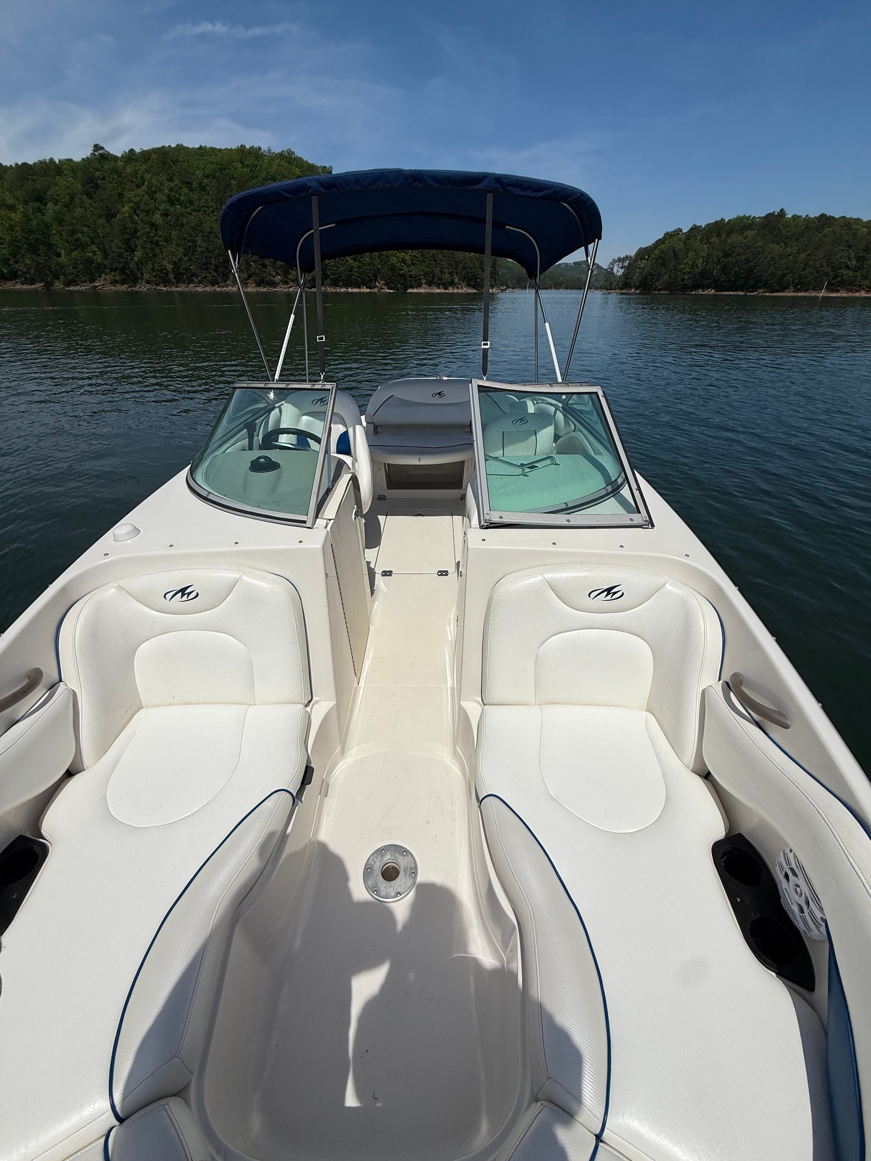 A white boat with blue accents and a blue sunshade on a calm lake.