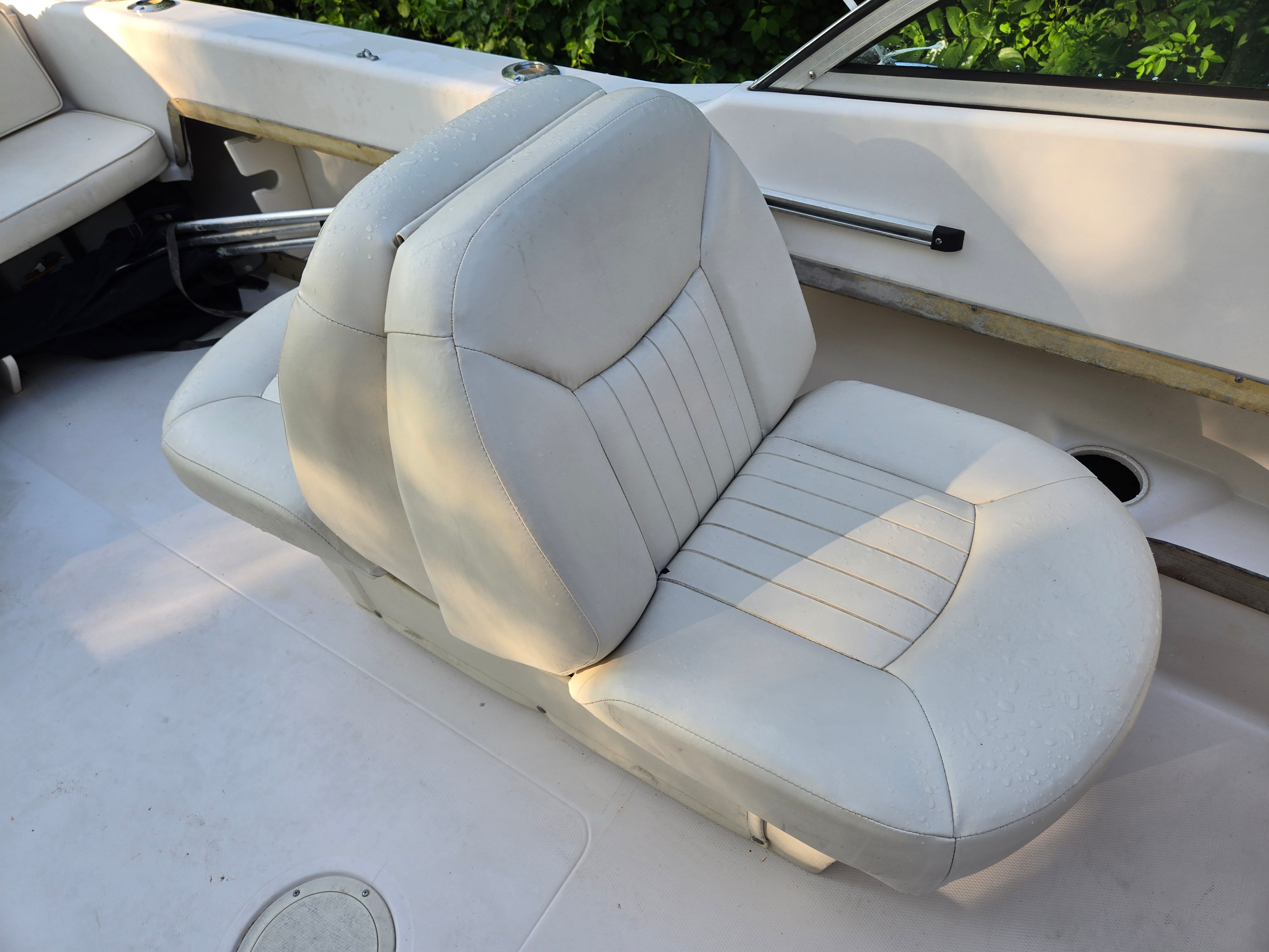 A white double seat on a boat with green foliage in the background.