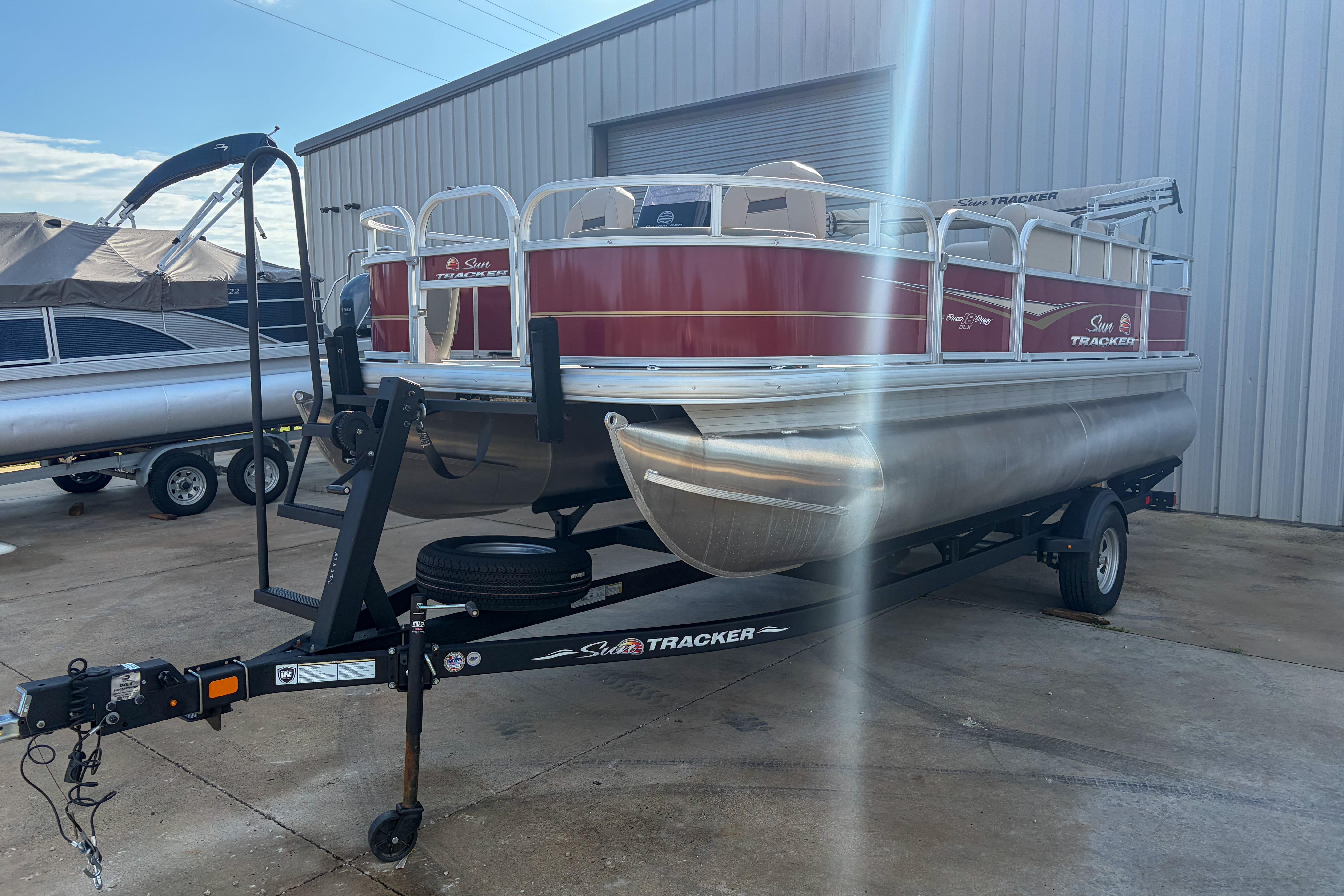 2024 Sun Tracker Bass Buggy 18 DLX pontoon boat on trailer, parked outdoors.