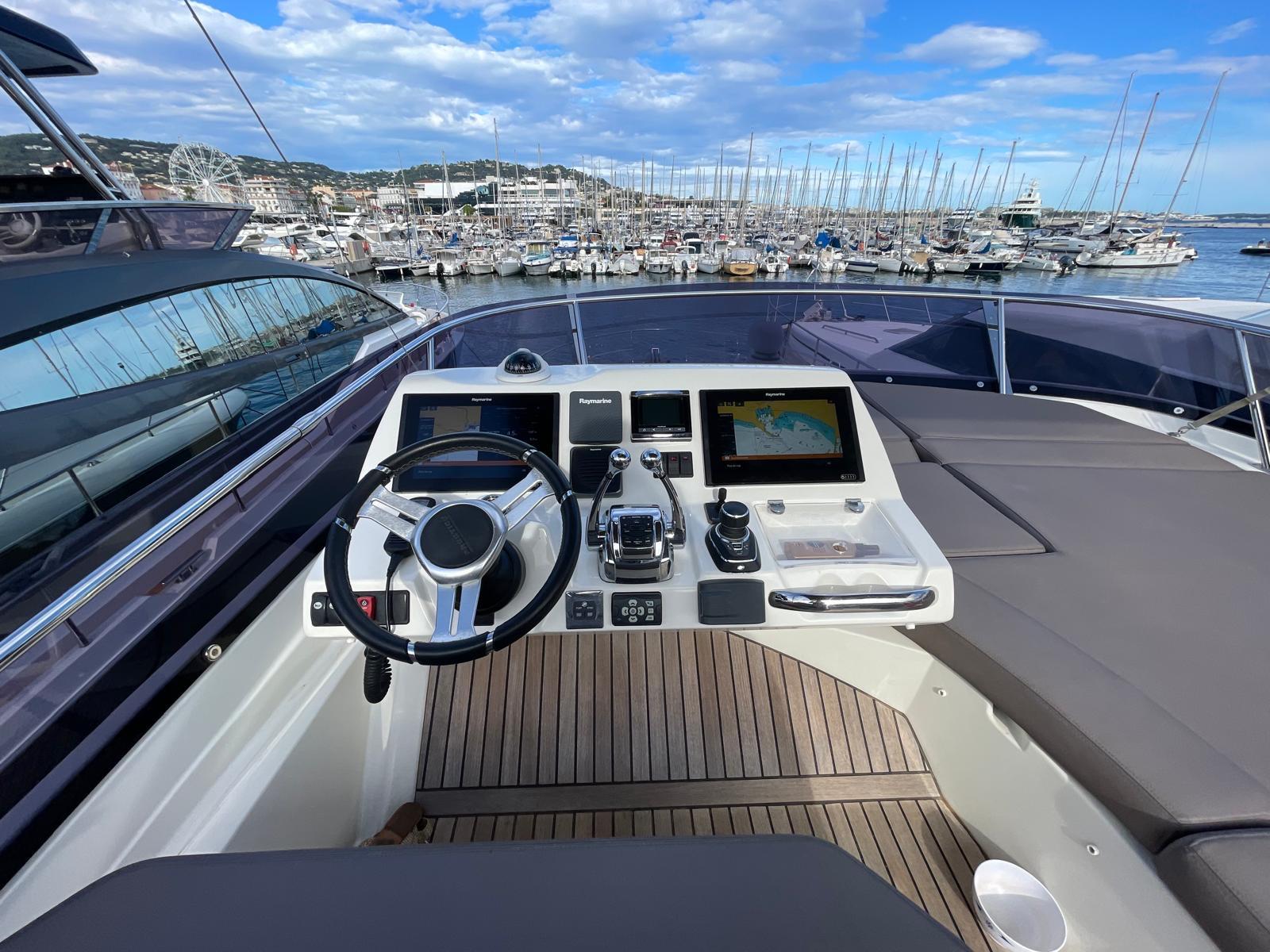 Helm of 2018 Prestige 560 yacht with marina view and clear blue sky.