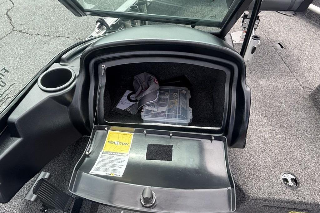 Open storage compartment in a 2021 Lund 1675 Adventure Sport boat, containing a cap and tackle box.
