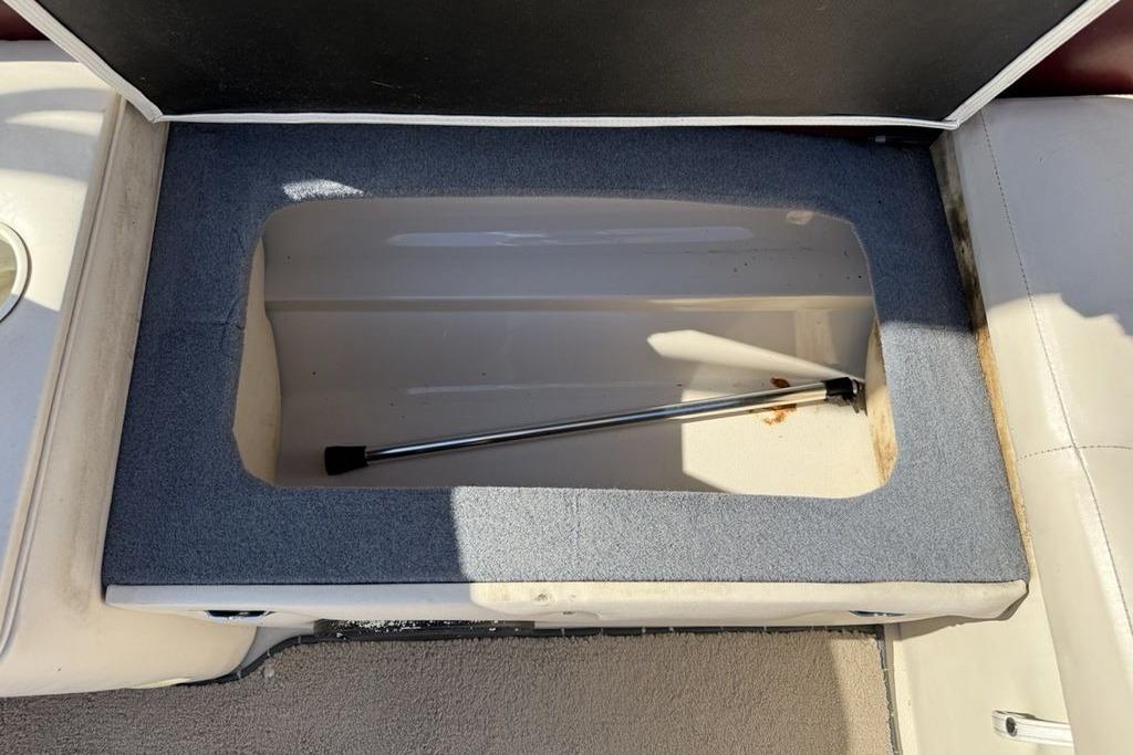 Open storage compartment in a 1999 Glastron GT 225 boat, featuring a hydraulic support rod.