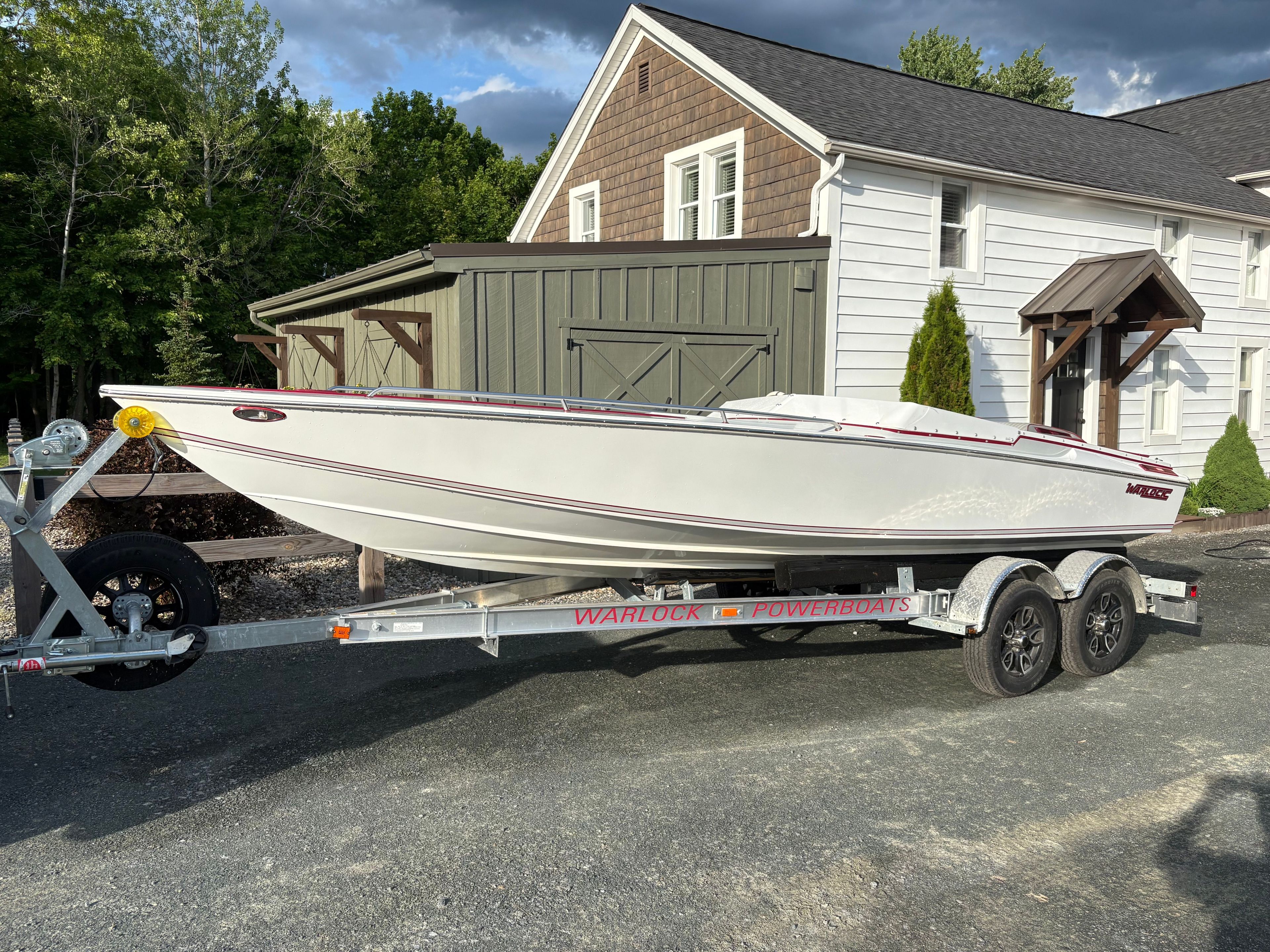 A white 1986 Warlock 23 boat on a trailer in front of a building.