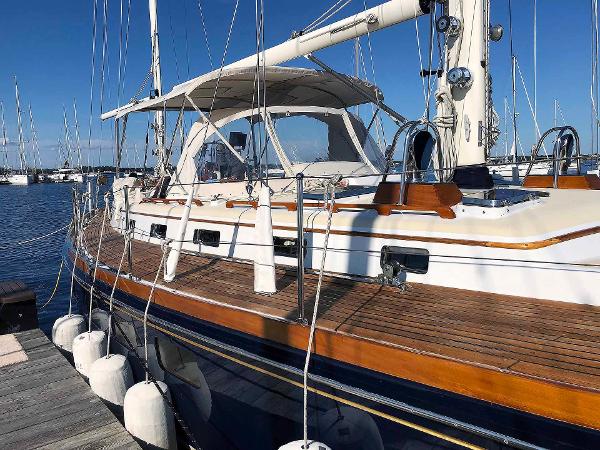 An elegant sailboat with a wooden deck docked, surrounded by other boats in the harbor.