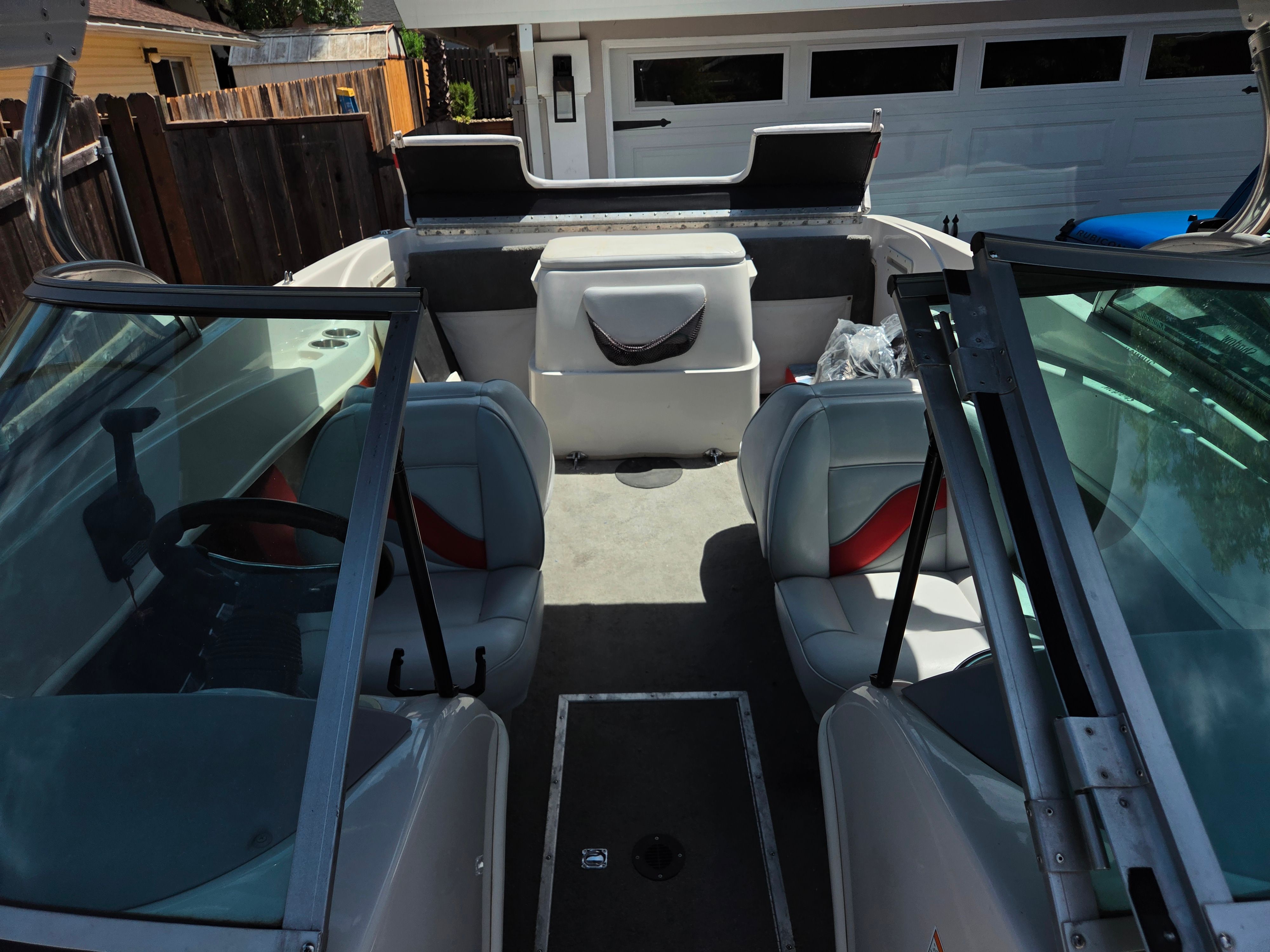 Interior view of a boat with gray seats and steering wheel, parked in a driveway.