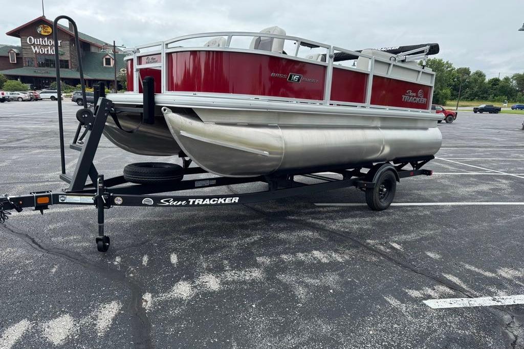 2026 Sun Tracker Bass Buggy 16 XL Select pontoon boat on trailer in parking lot.