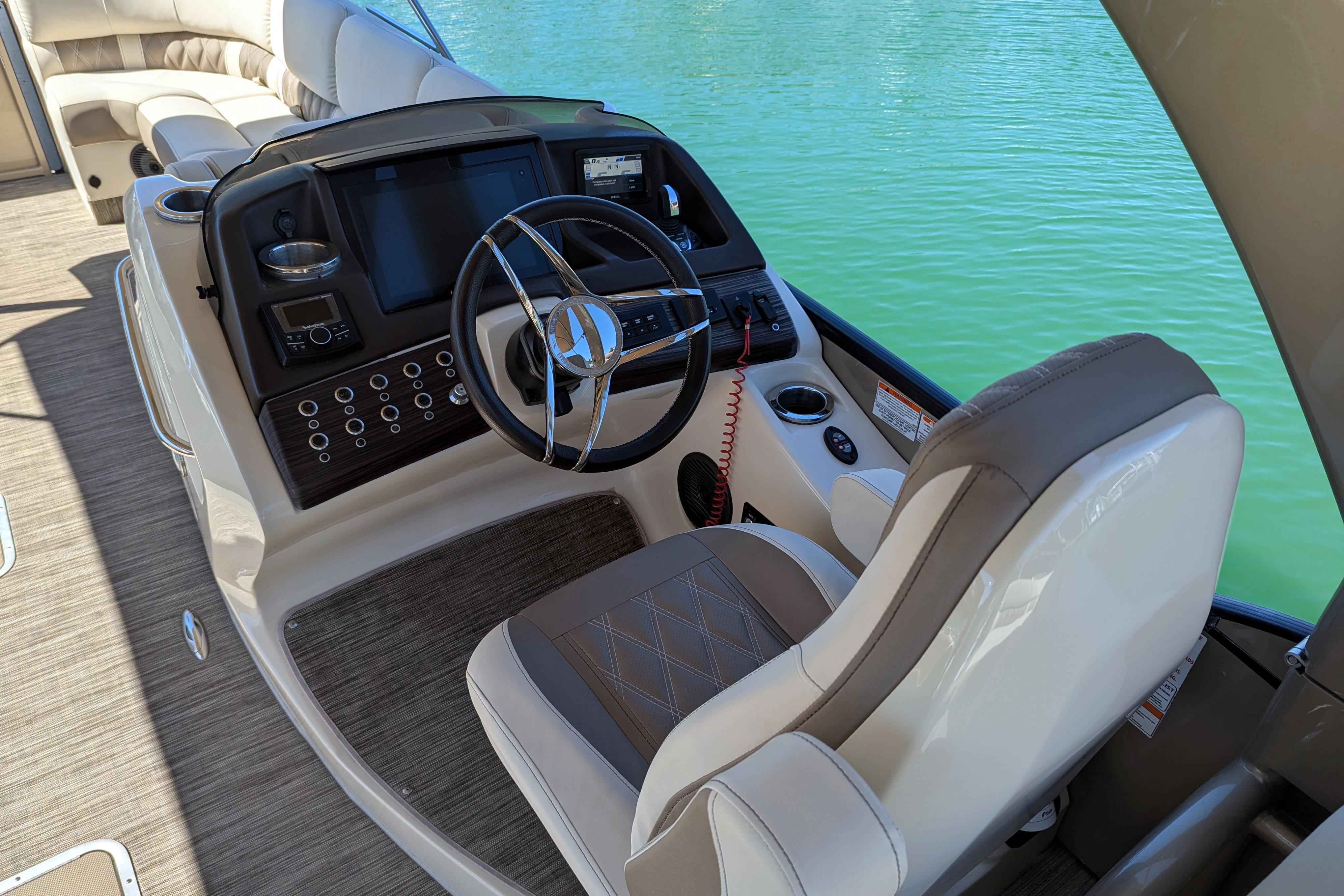 2022 Bennington QXFBAX2 boat helm with steering wheel and control panel on water.