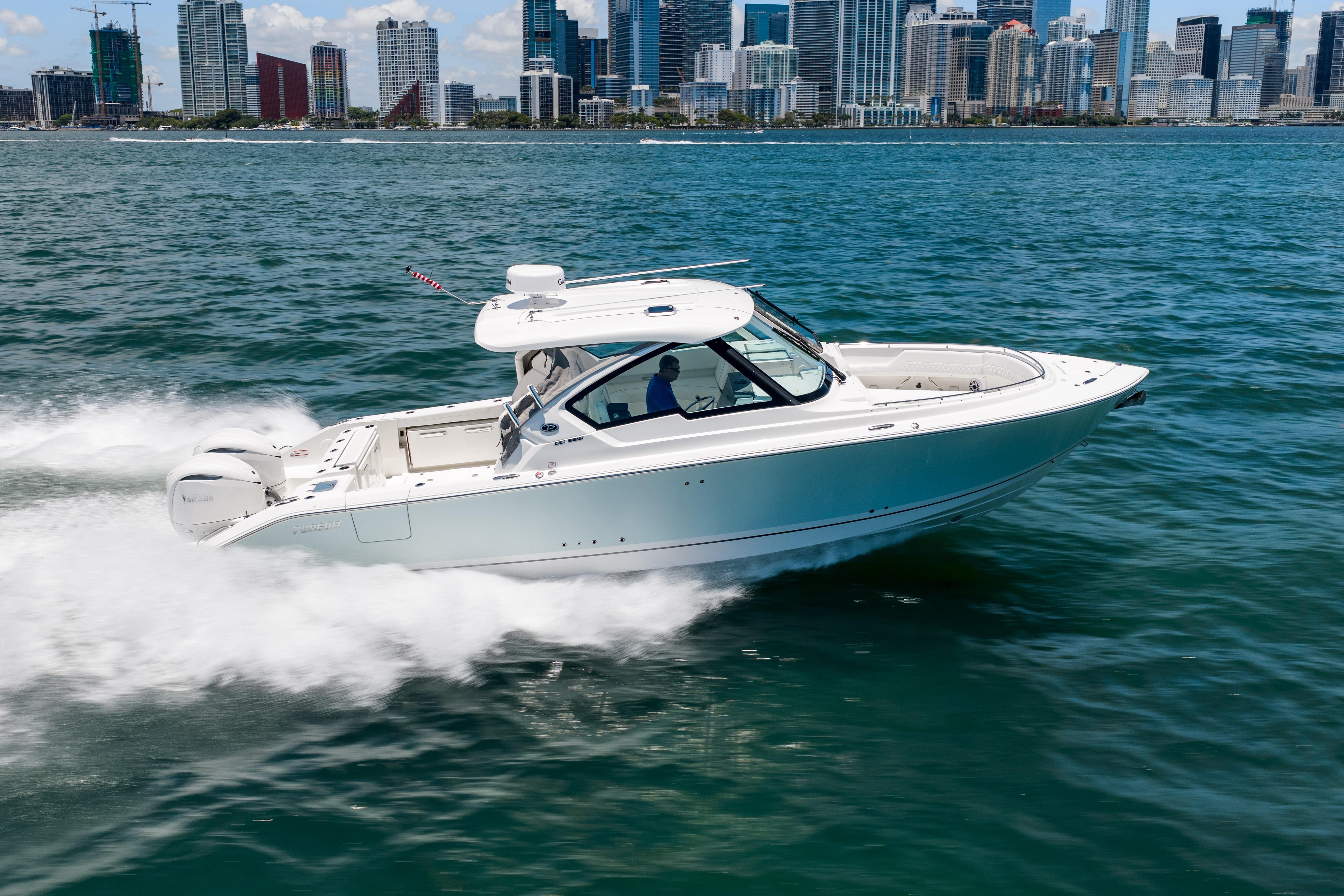 2026 Pursuit DC 326 Dual Console boat cruising on water with city skyline backdrop.