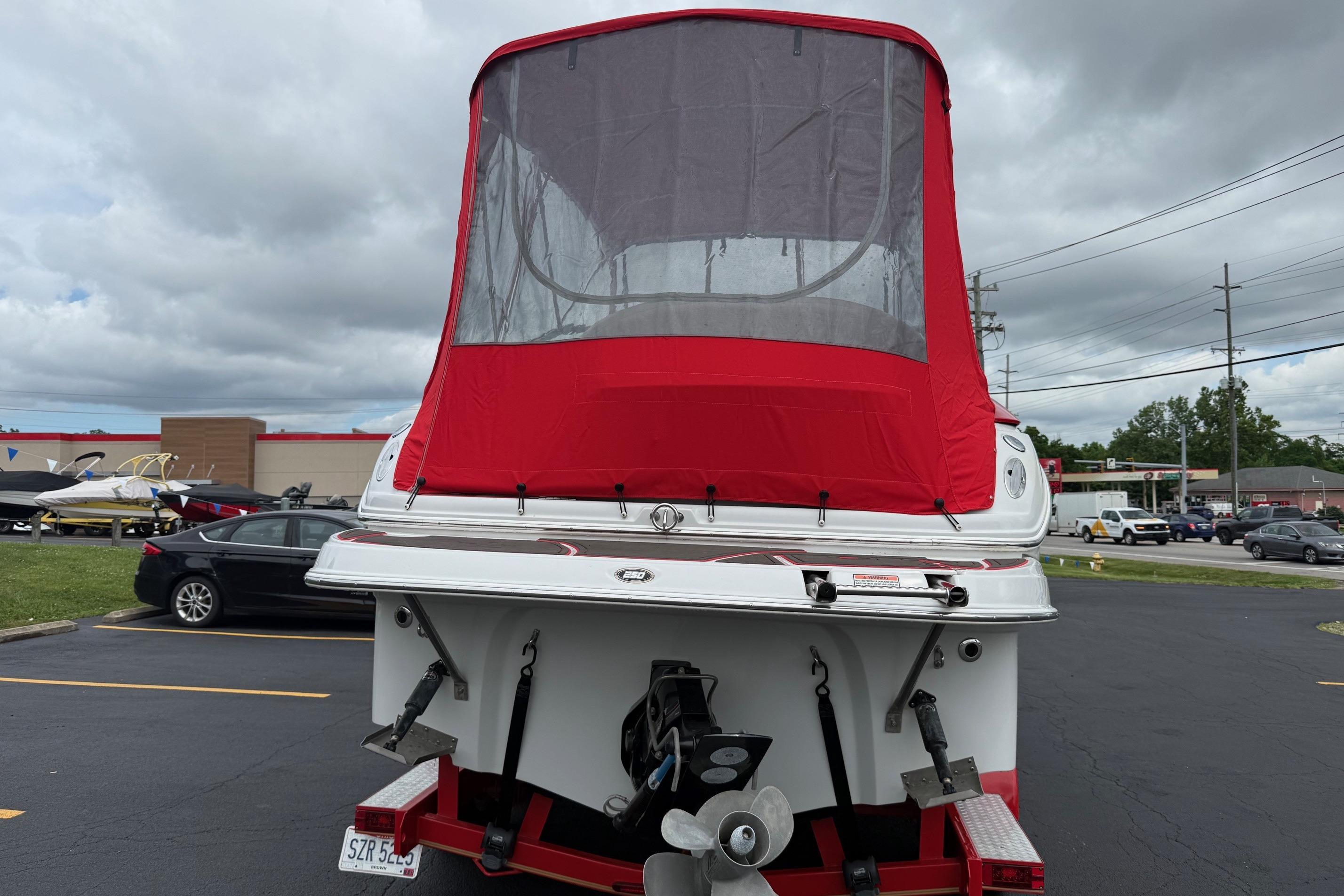 2005 Crownline 250 CR boat with red canopy, parked in a lot under cloudy skies.