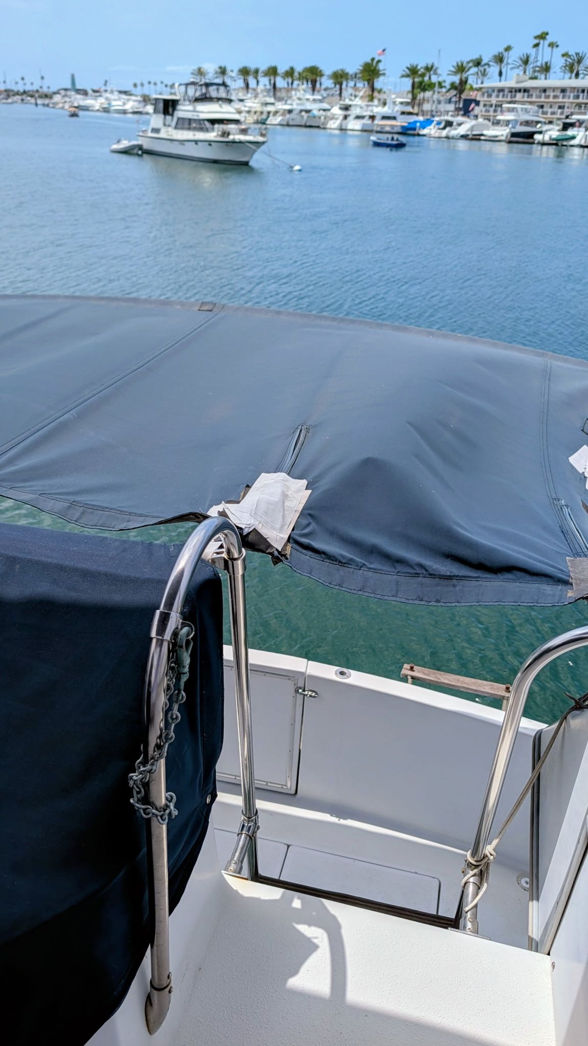 View from a boat with a blue cover overlooking a calm harbor with several boats.