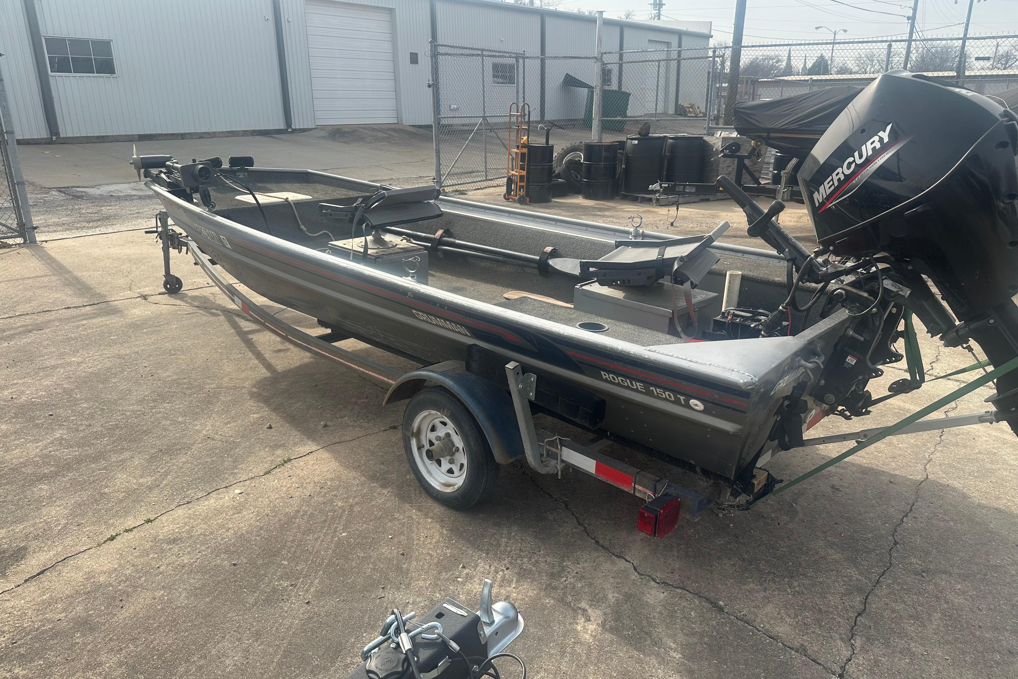 1991 Grumman Rogue 150 T boat with Mercury engine on trailer in industrial setting.