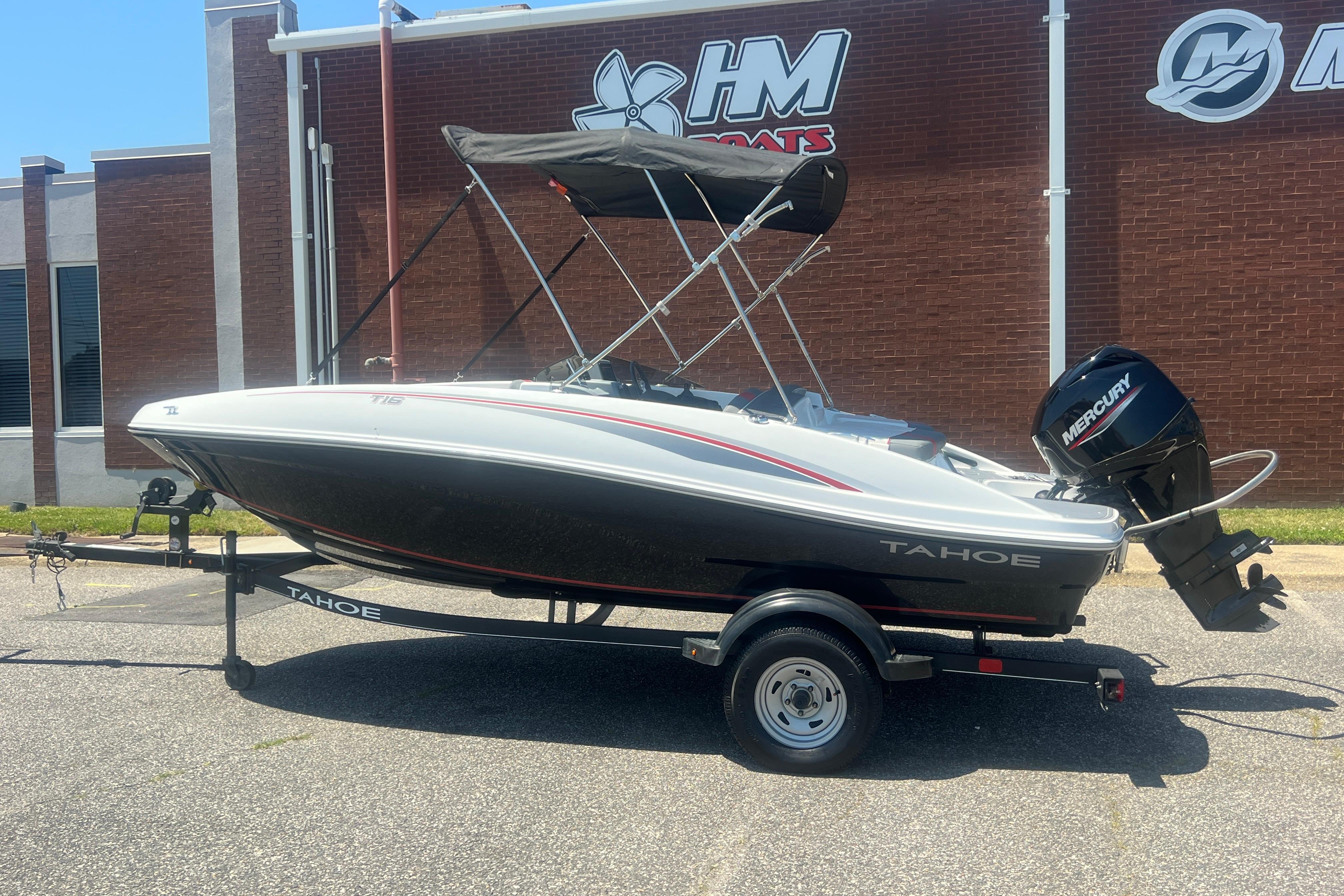 2023 Tahoe T16 boat with Mercury engine on trailer, parked outside a building.
