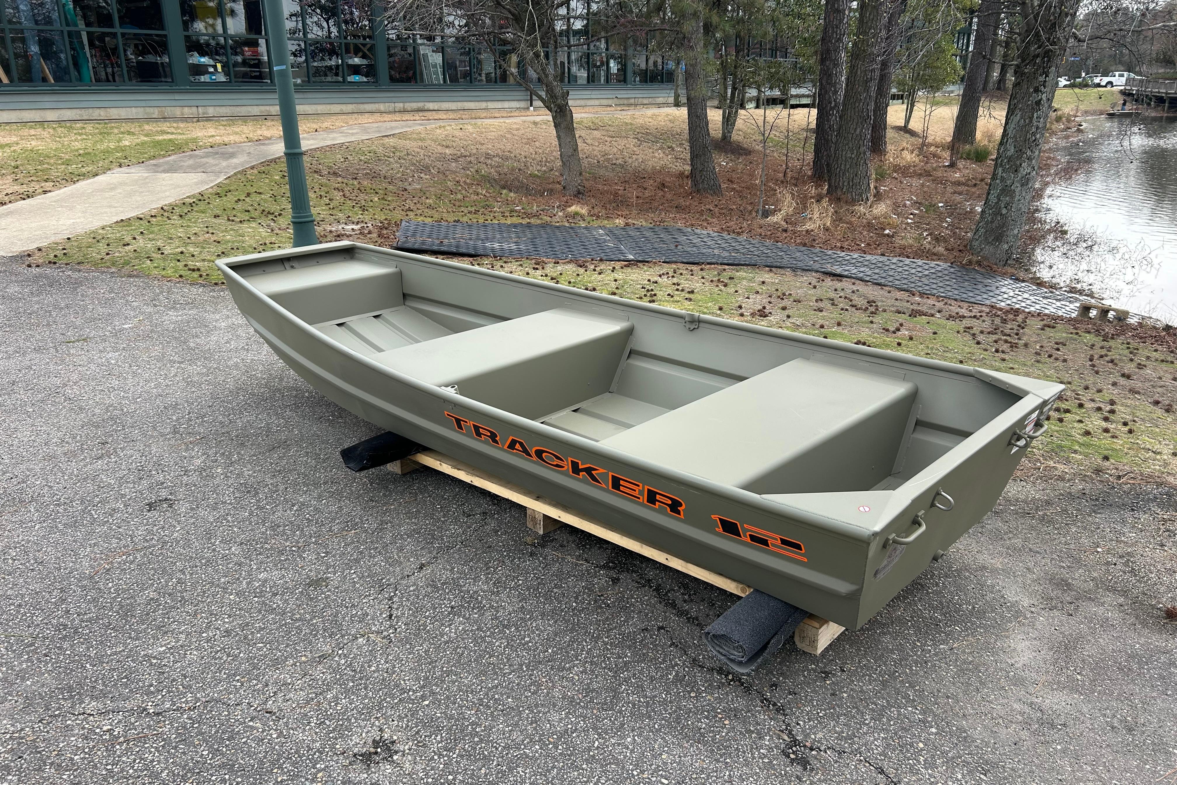 2026 Tracker Grizzly 12 Jon boat on pavement near a pond and trees.