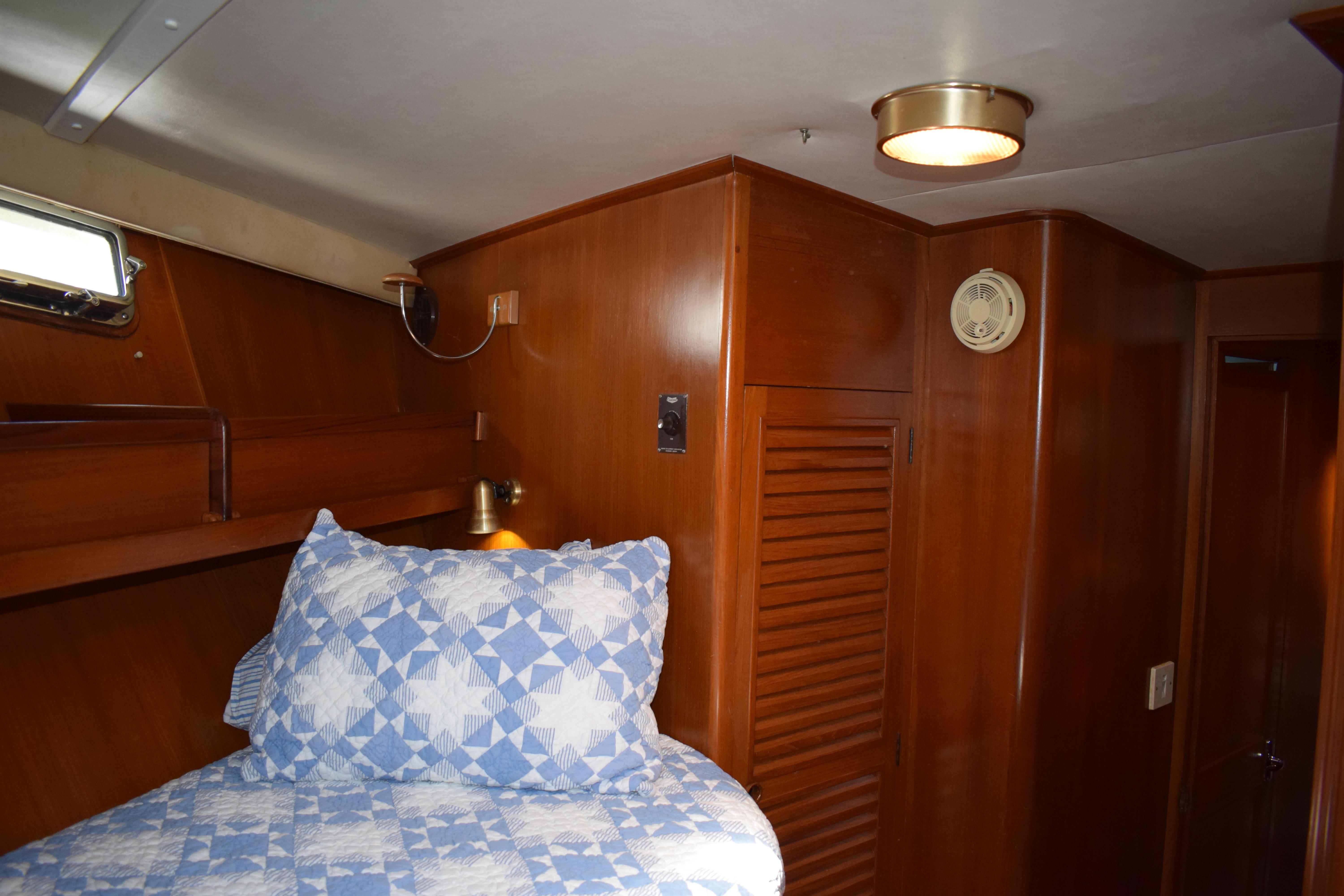 Cozy cabin interior of 1980 Cheoy Lee 52 Motorsailer with wooden paneling and blue quilted bedding.