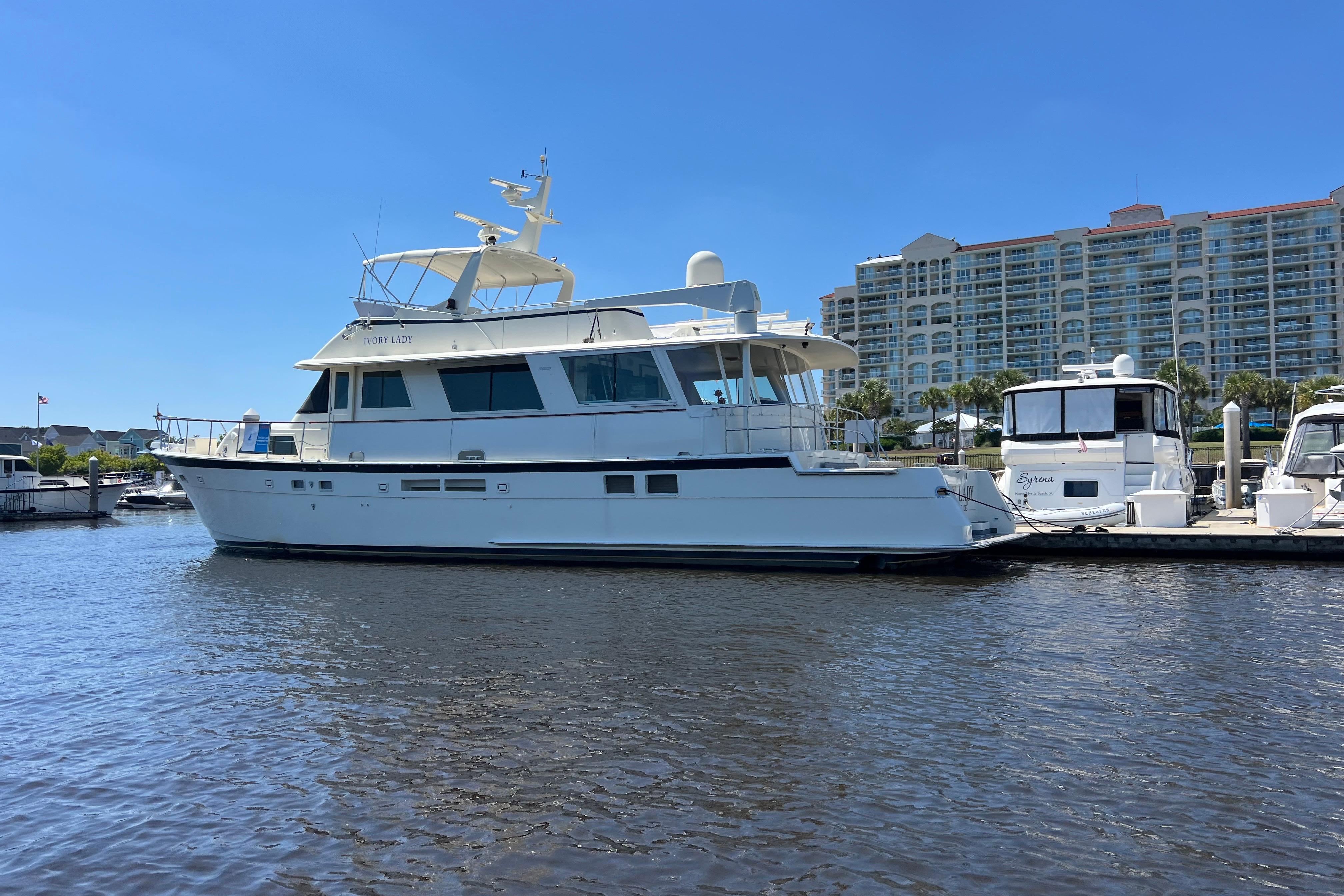 1987 Hatteras 70 Cockpit Motor Yacht docked at marina under clear blue sky.