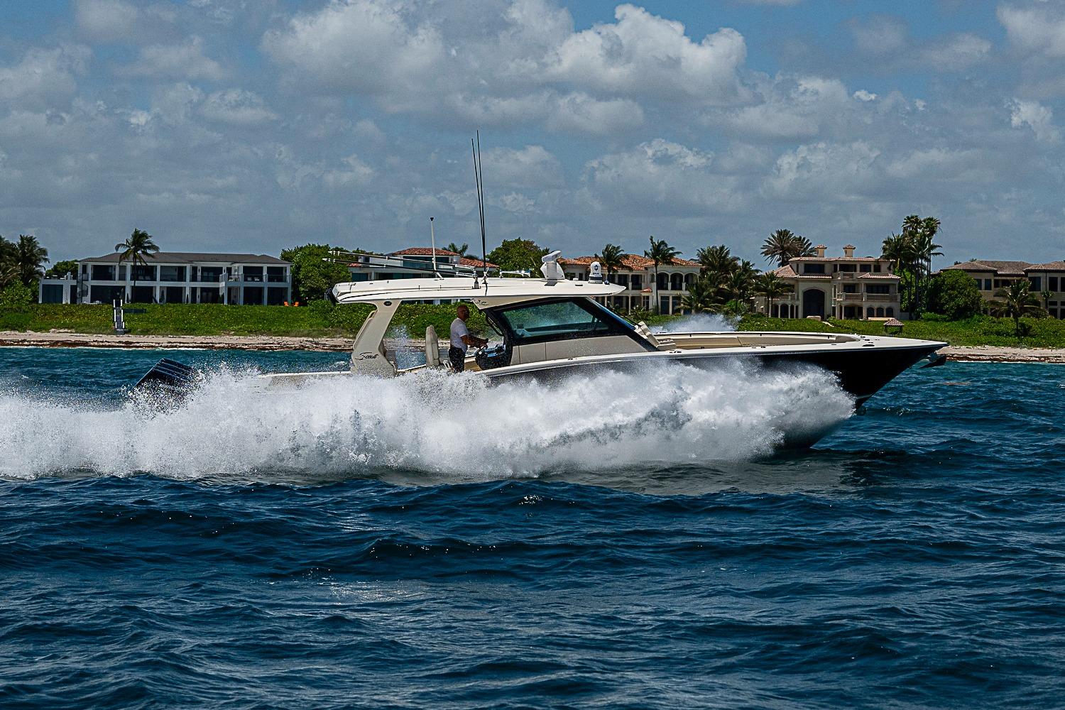 2025 Scout 425 LXF boat cruising on ocean near luxury waterfront homes.