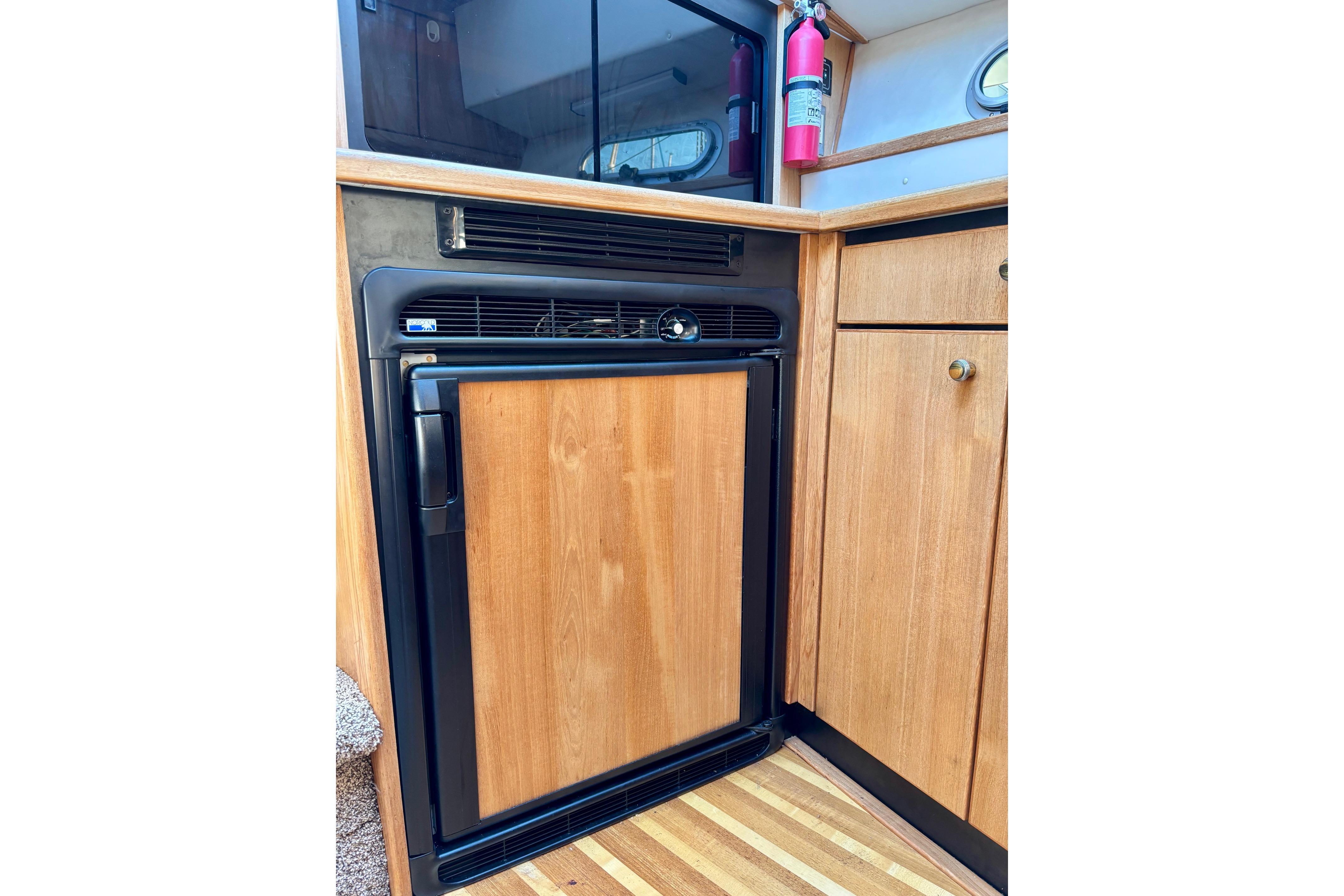 1998 Bayliner 3388 Command Bridge Motoryacht interior with wooden cabinetry and compact refrigerator.