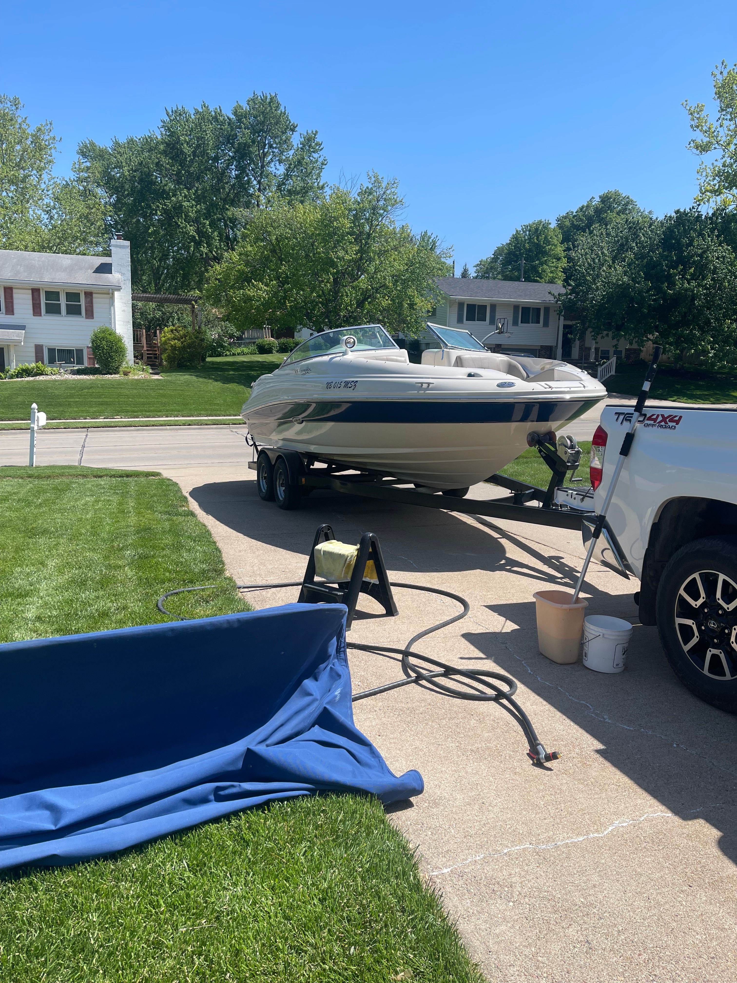 A Sea Ray 220 Sundeck boat is on a trailer in a residential street.