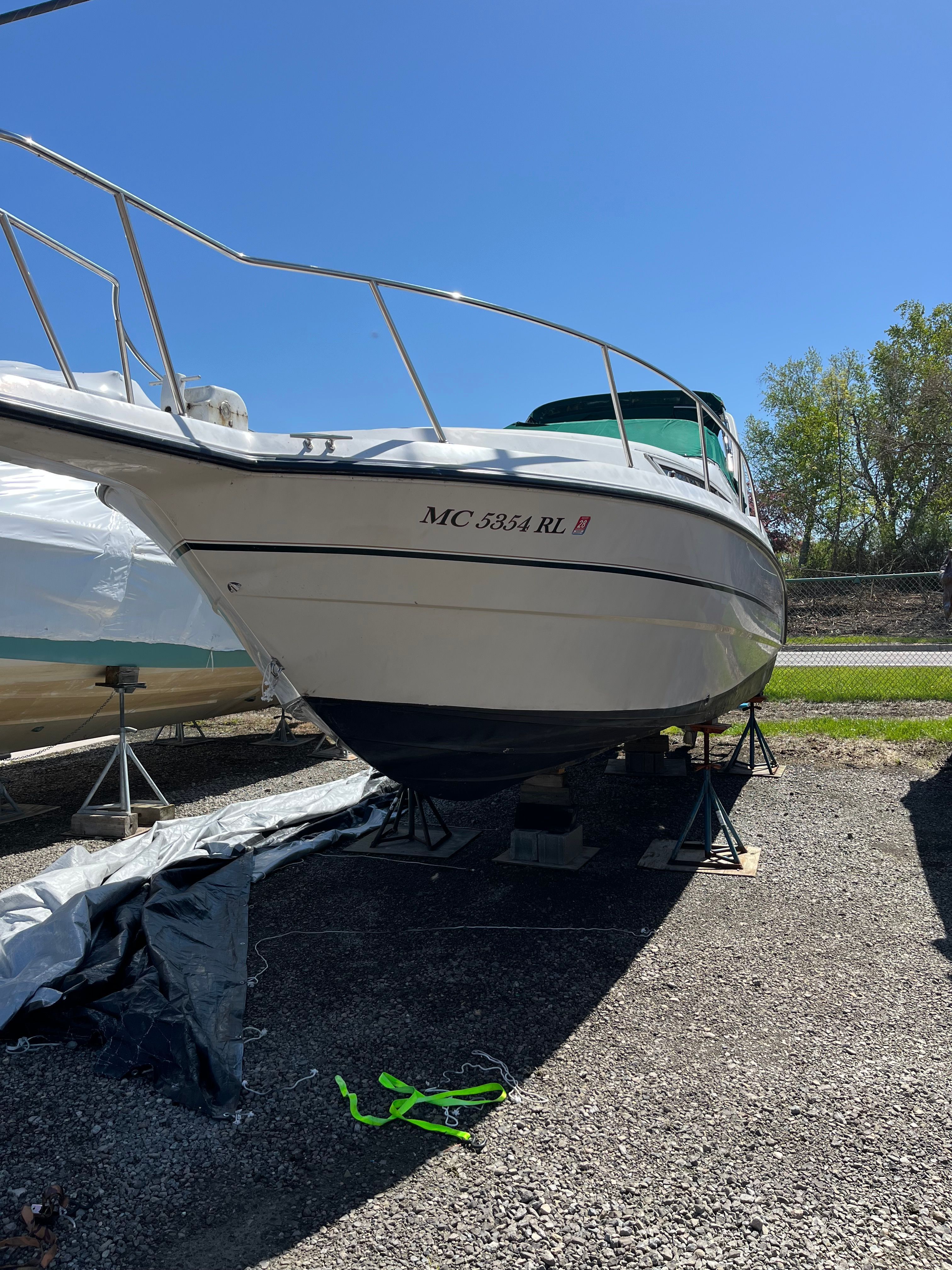 A white boat on a dry dock, supported by metal stands, with a blue sky in the background.
