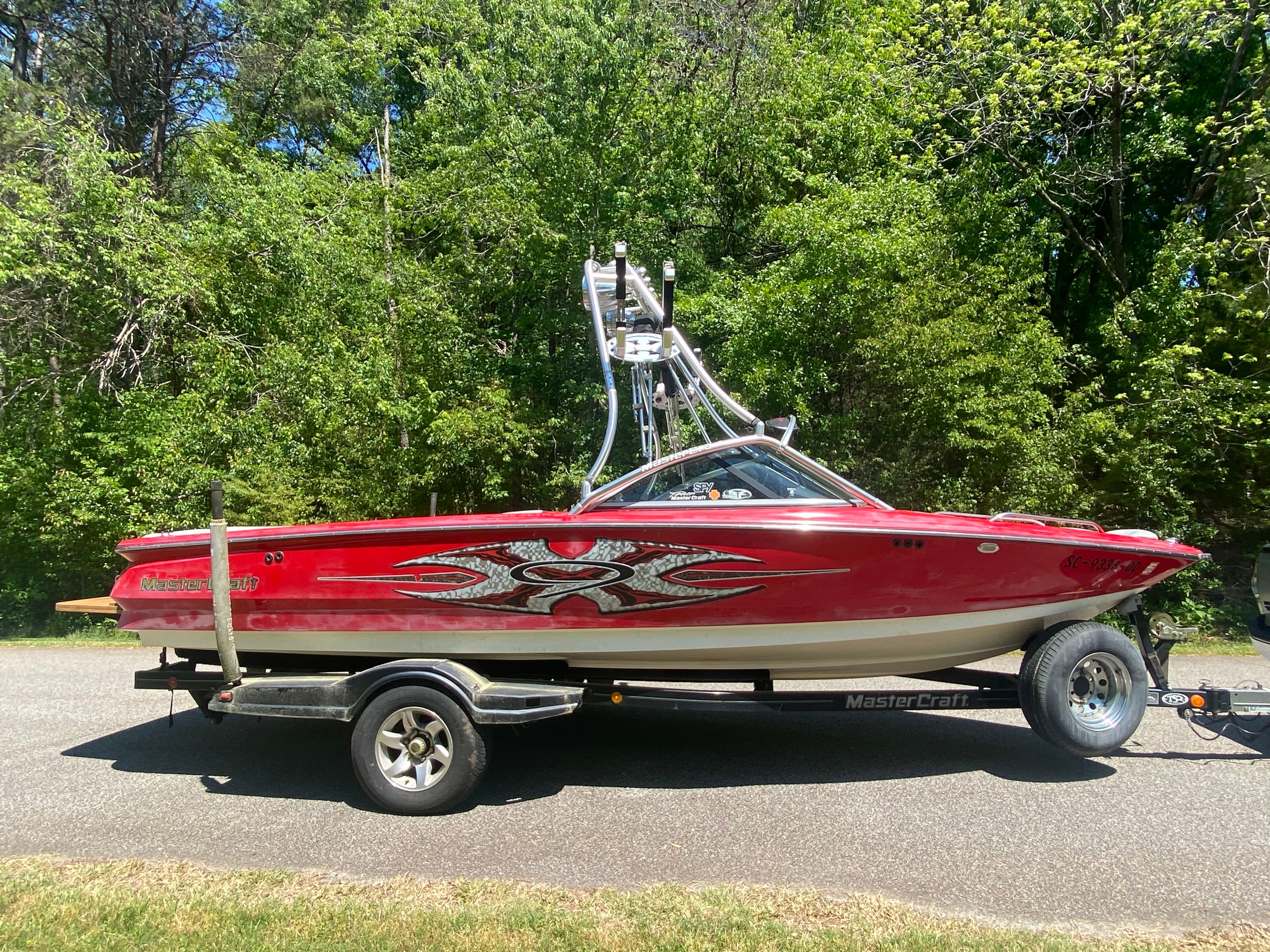 A red 2004 MasterCraft X-9 boat on a trailer, set against a wooded background.