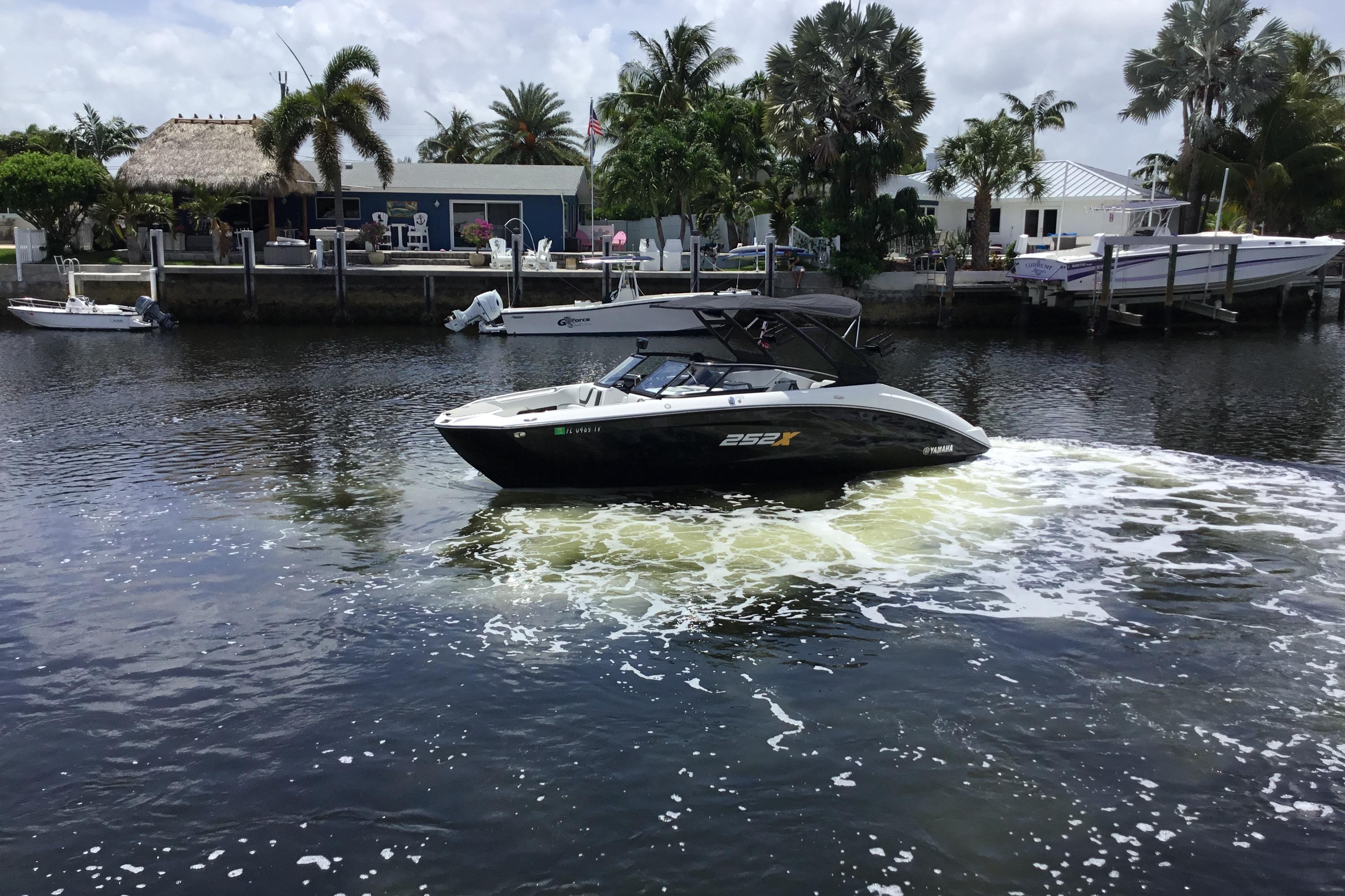 2023 Yamaha Boats 252XE cruising on a scenic waterway with palm trees in the background.