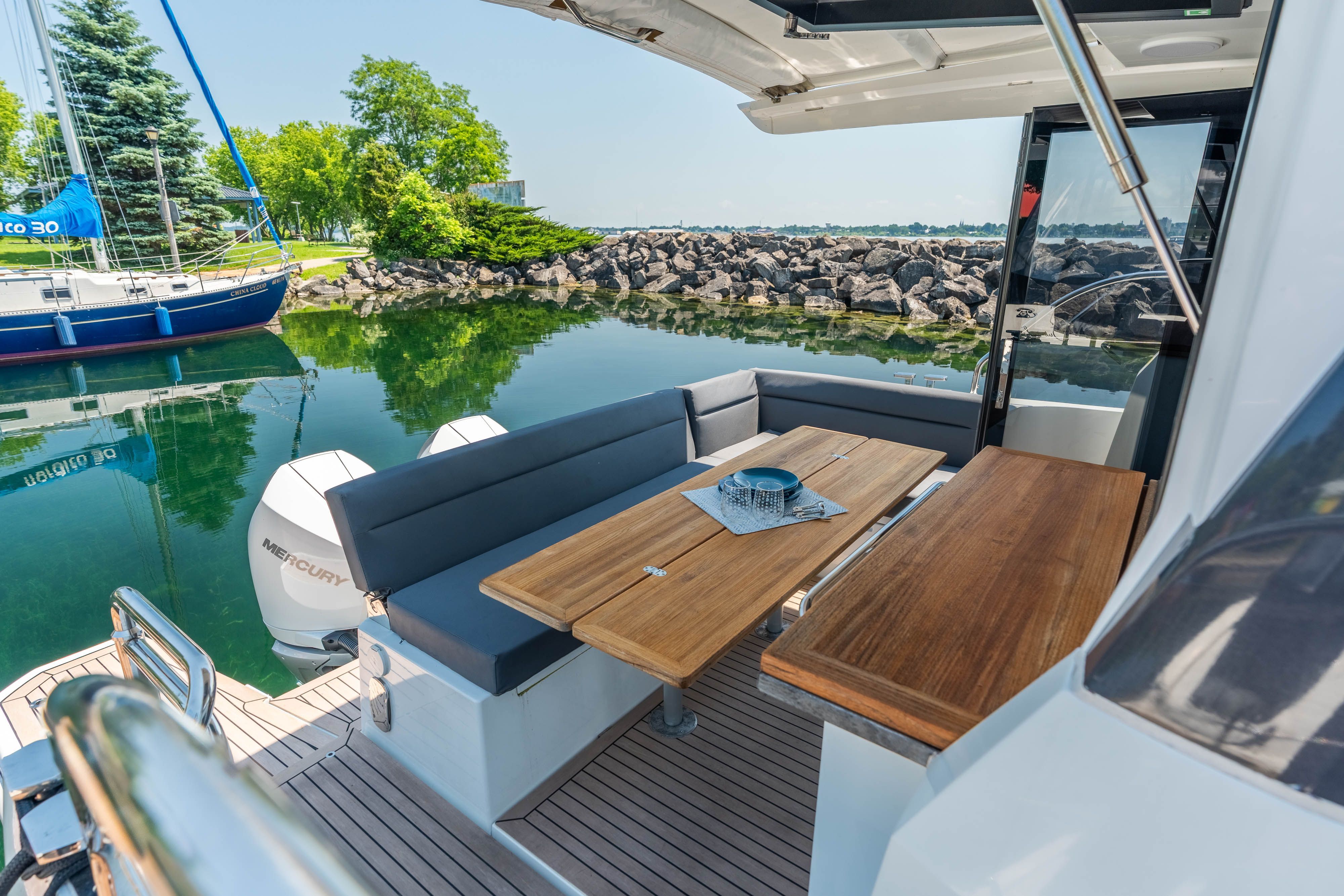 The image shows the aft of a 2023 Sealine C335V with a sleek seating area and wooden table.