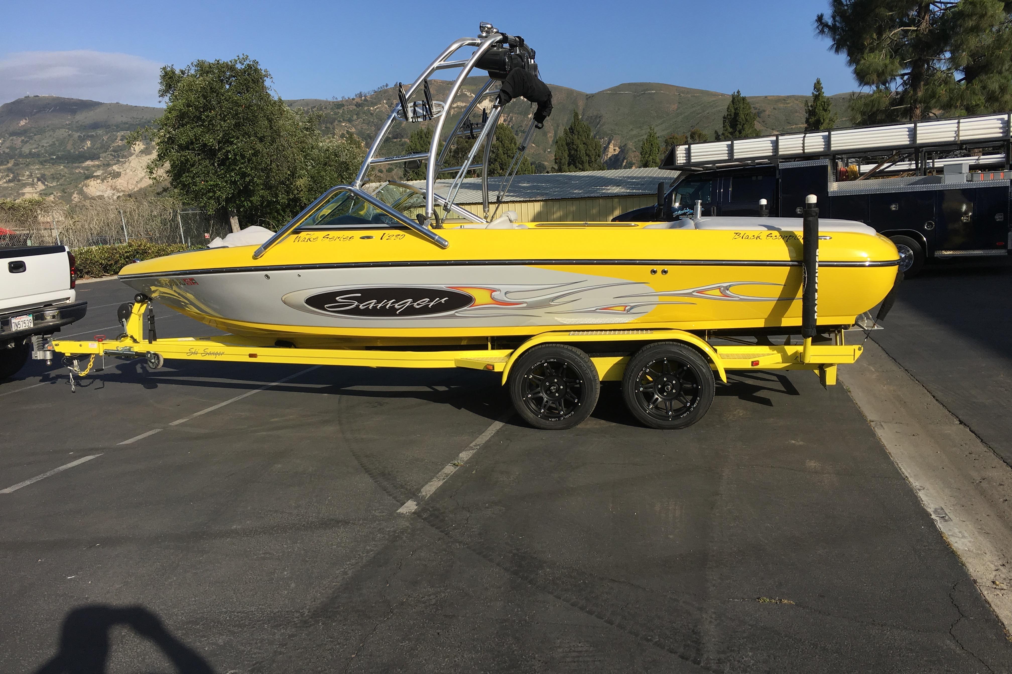 Yellow 2006 Sanger V230 boat on trailer, parked outdoors with scenic mountain backdrop.